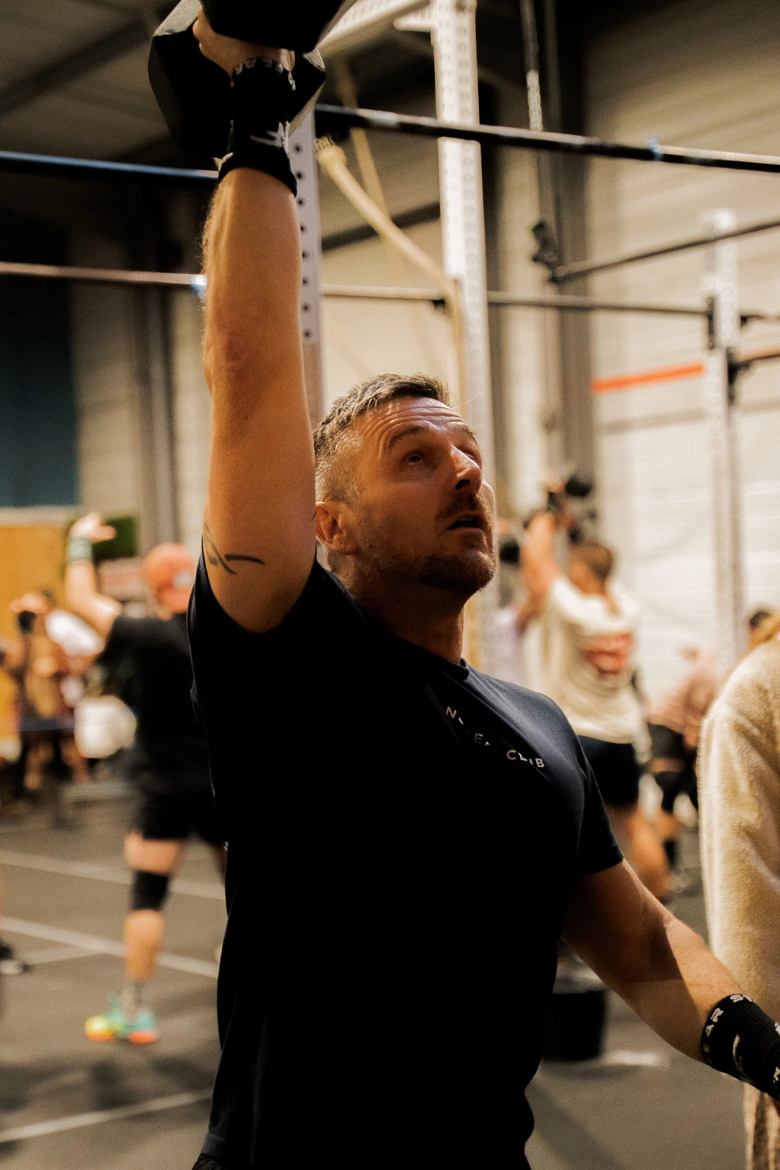 Homme levant une barre de musculation dans une salle de sport occupée par plusieurs personnes