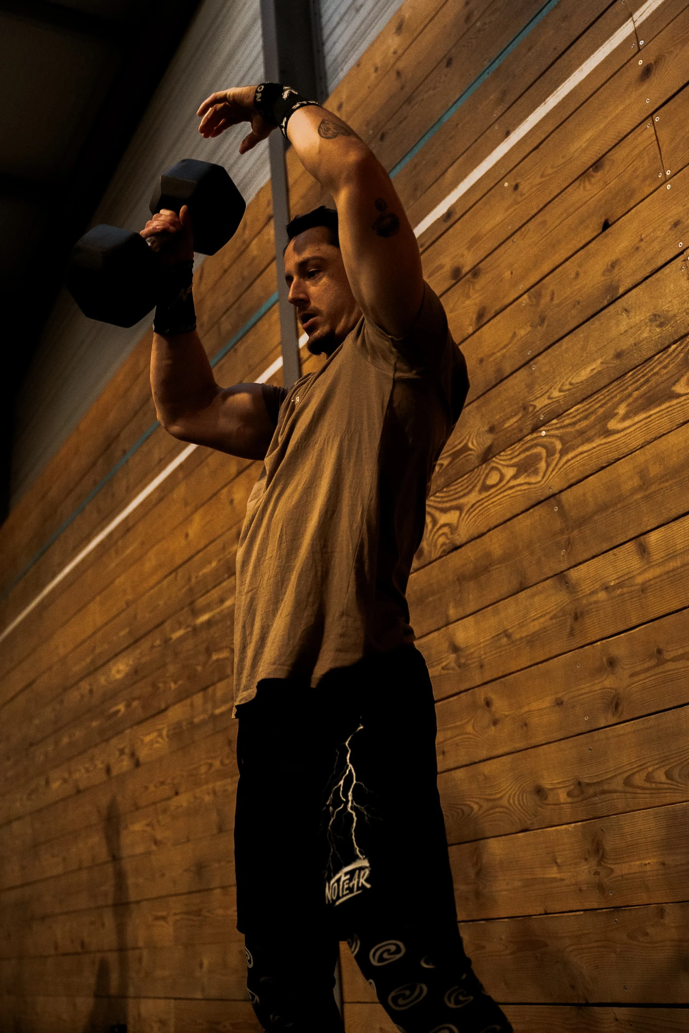 Un homme en train de faire de l'exercice avec un haltère dans une salle de sport en bois.