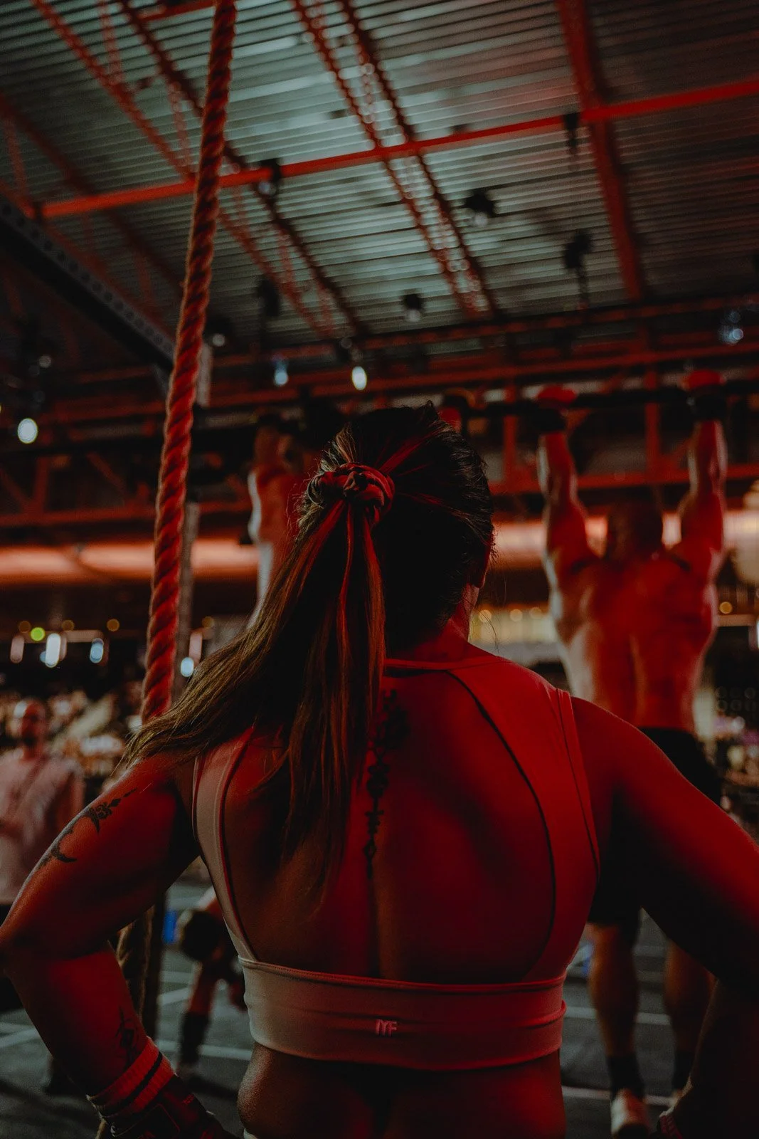 Femme regardant un athlète suspendu à une barre dans une salle CrossFit sombre — photographe CrossFit Voar by Tim