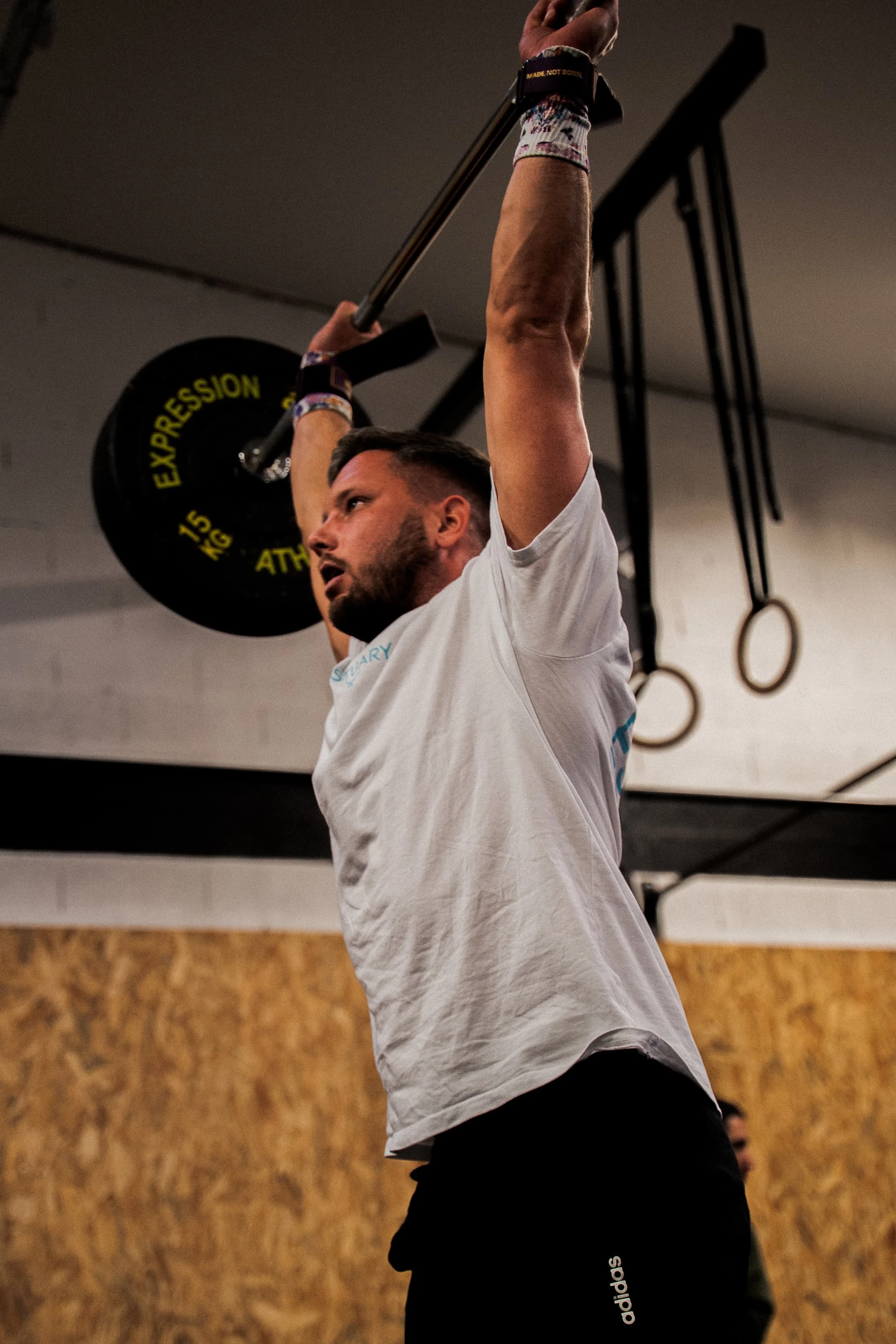 Un homme en train de soulever une barre avec des poids dans une salle de sport, équipée de ring de gymnastique suspendus.