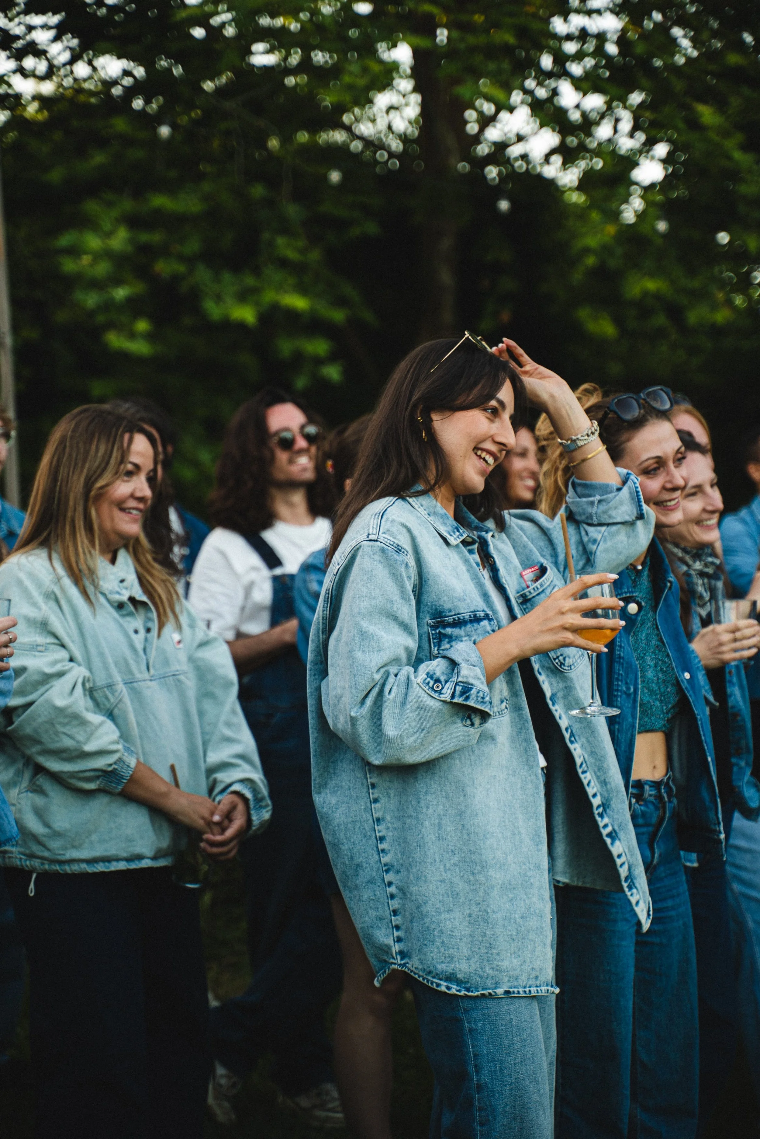 Groupe de jeunes femmes souriantes lors d'un événement en plein air, portant des vêtements décontractés en jean, avec des arbres en arrière-plan.