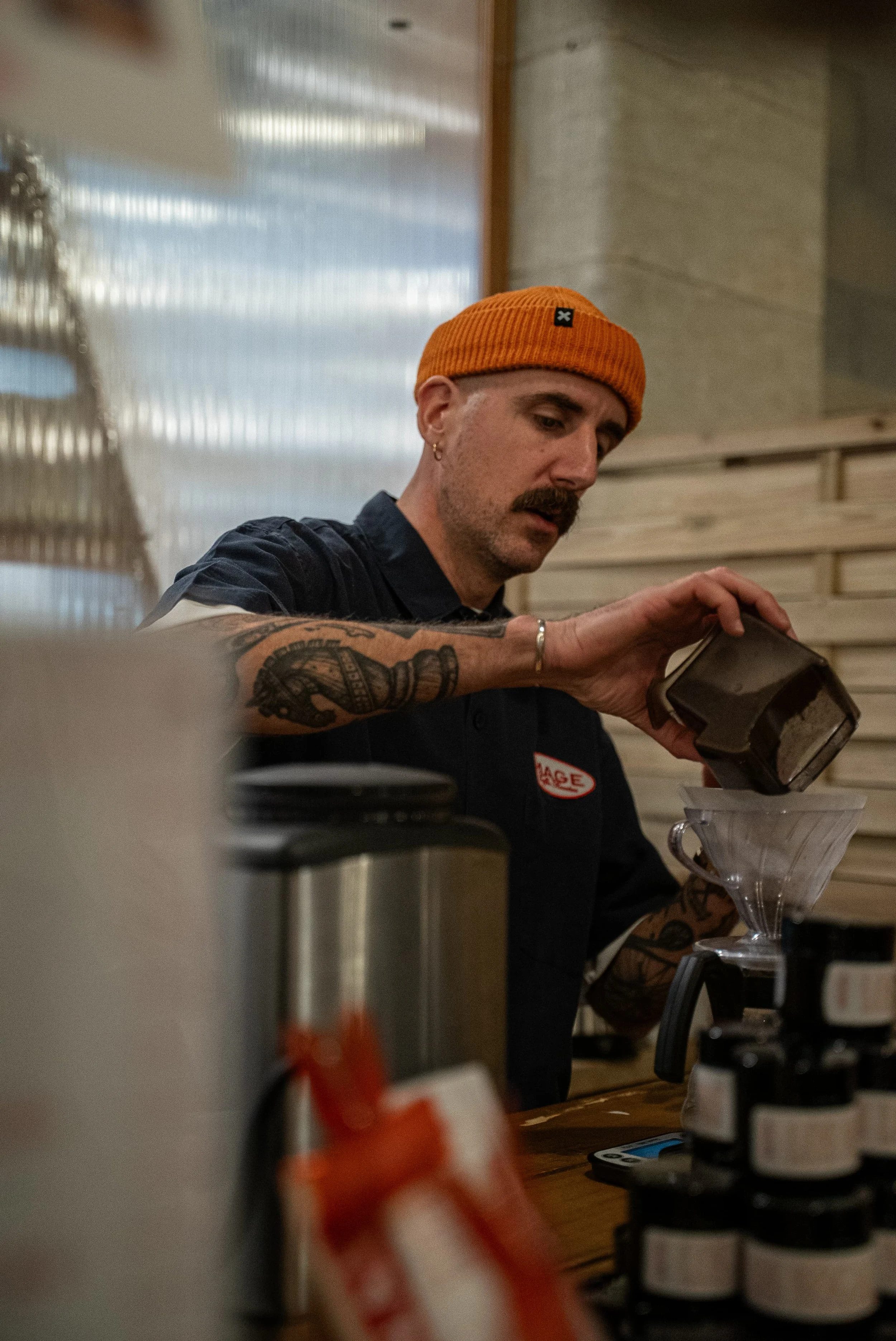 Un homme avec un chapeau orange et une moustache, utilisant une balance à filtre pour préparer une substance, dans un environnement de cuisine ou de laboratoire.