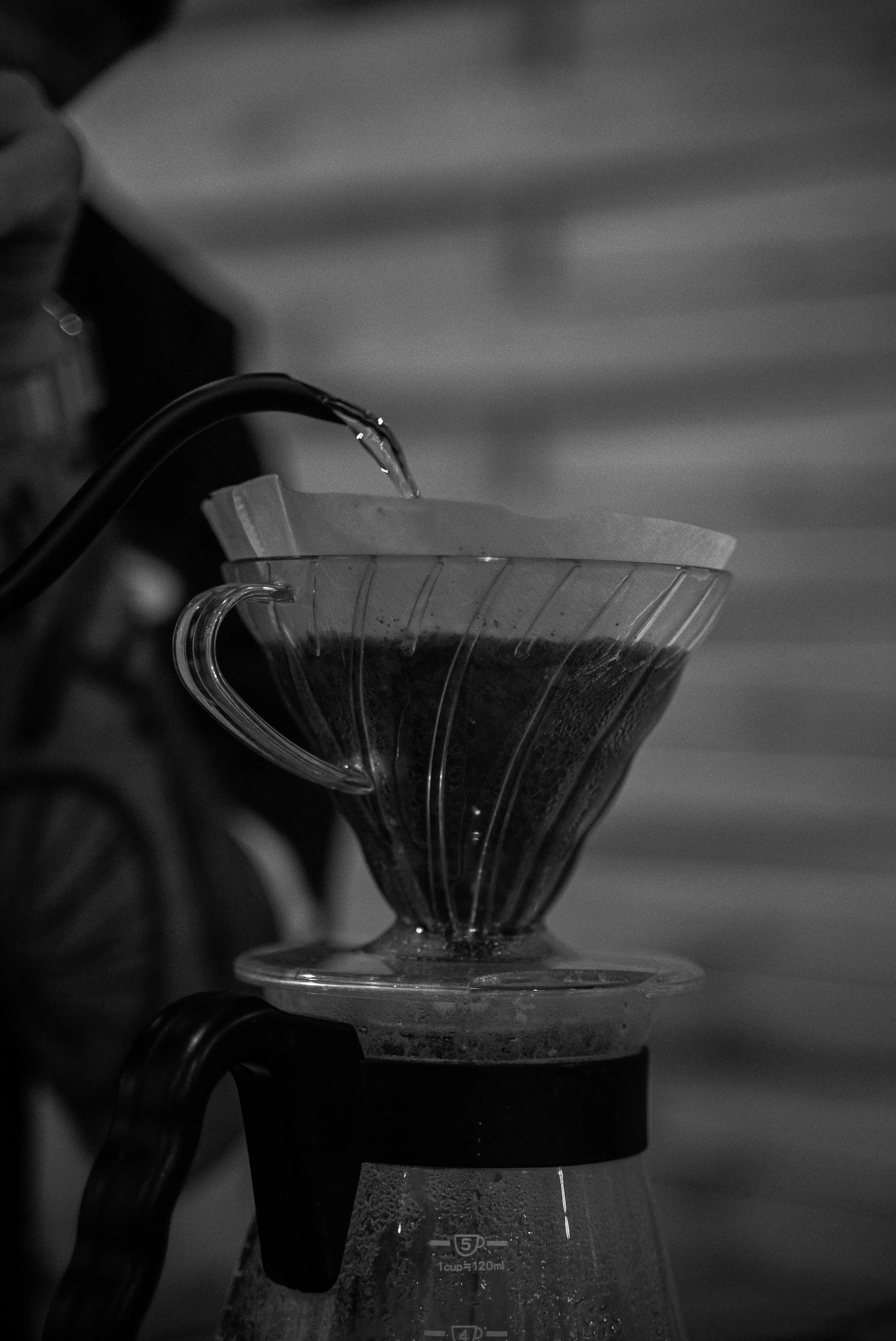 Une cafetière verse du café dans un filtre en papier et une tasse en verre transparente avec des mesures.