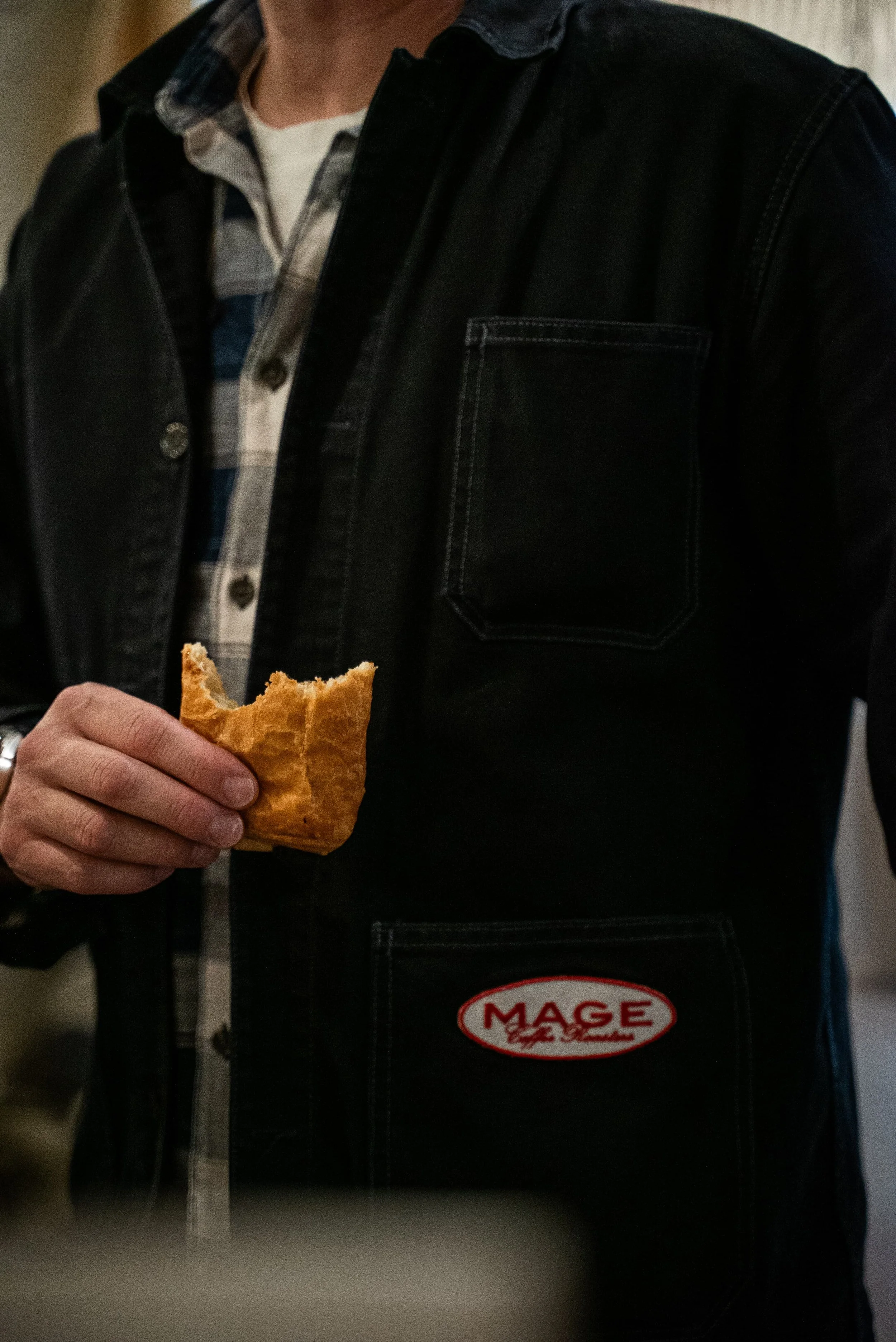 Personne portant une veste noire et une chemise à carreaux, tenant un croissant dans la main.