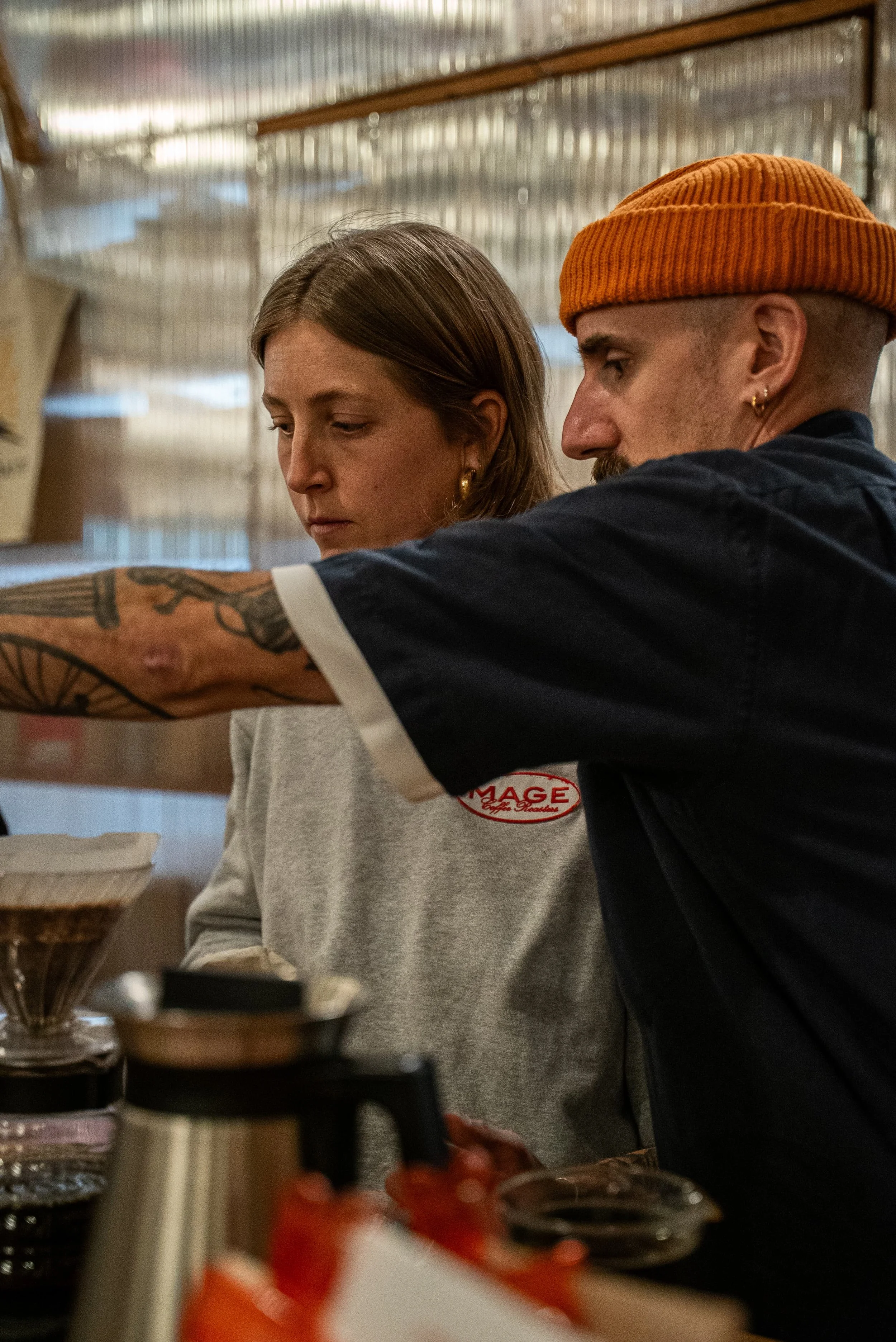 Deux personnes, un homme et une femme, travaillent derrière un comptoir dans une cuisine ou un café, concentrés sur leur tâche.