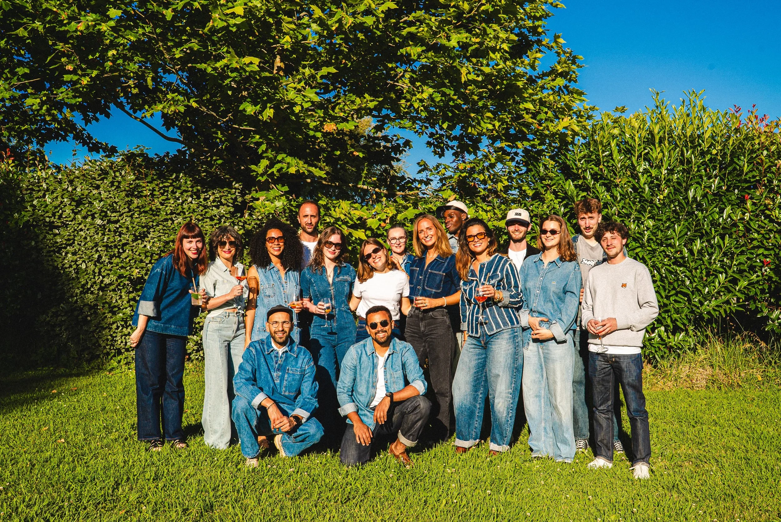 Un groupe de personnes posant pour une photo en plein air, devant des arbres verts et un ciel bleu, lors d'une journée ensoleillée.