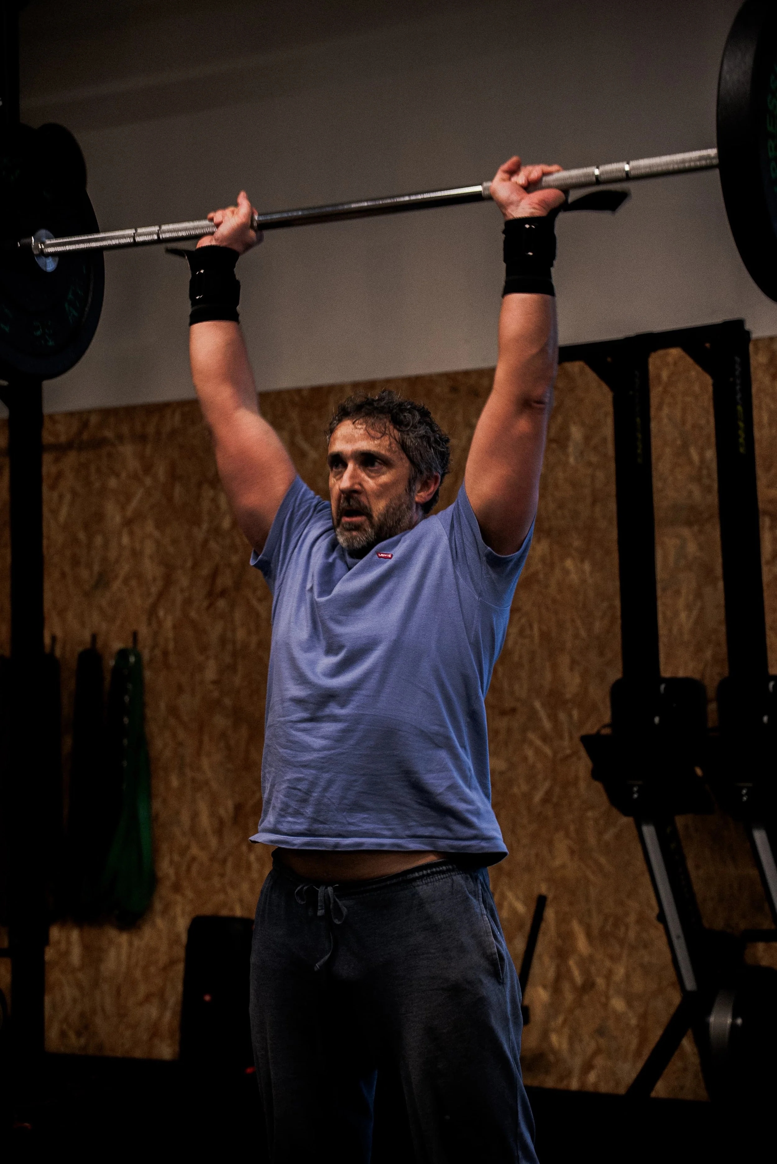 Un homme soulevant une barre avec des poids dans une salle de sport, portant un t-shirt bleu et des poignets de sports noirs.