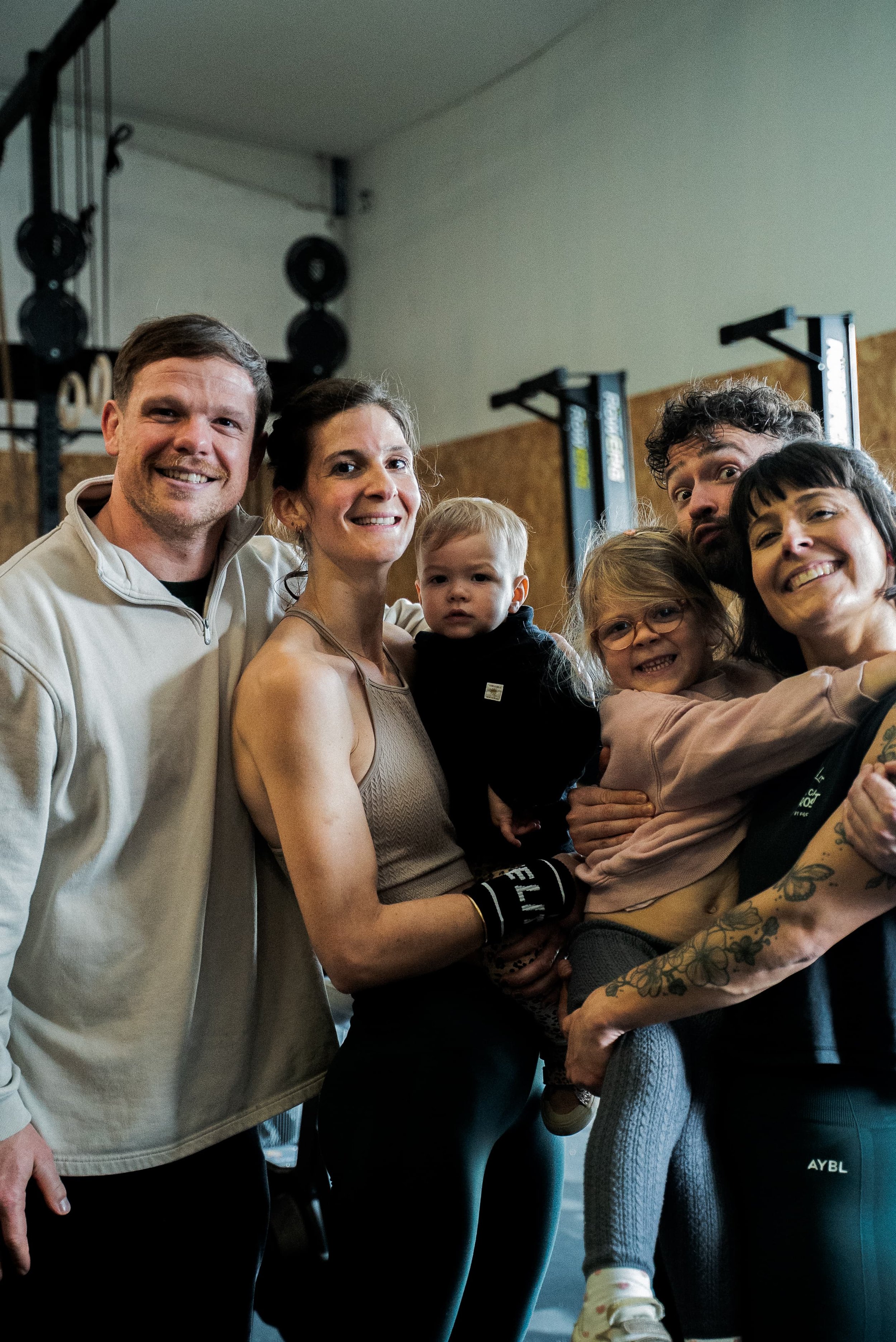 Groupe de personnes souriantes, y compris deux enfants, réunies dans une salle de sport ou gymnase.