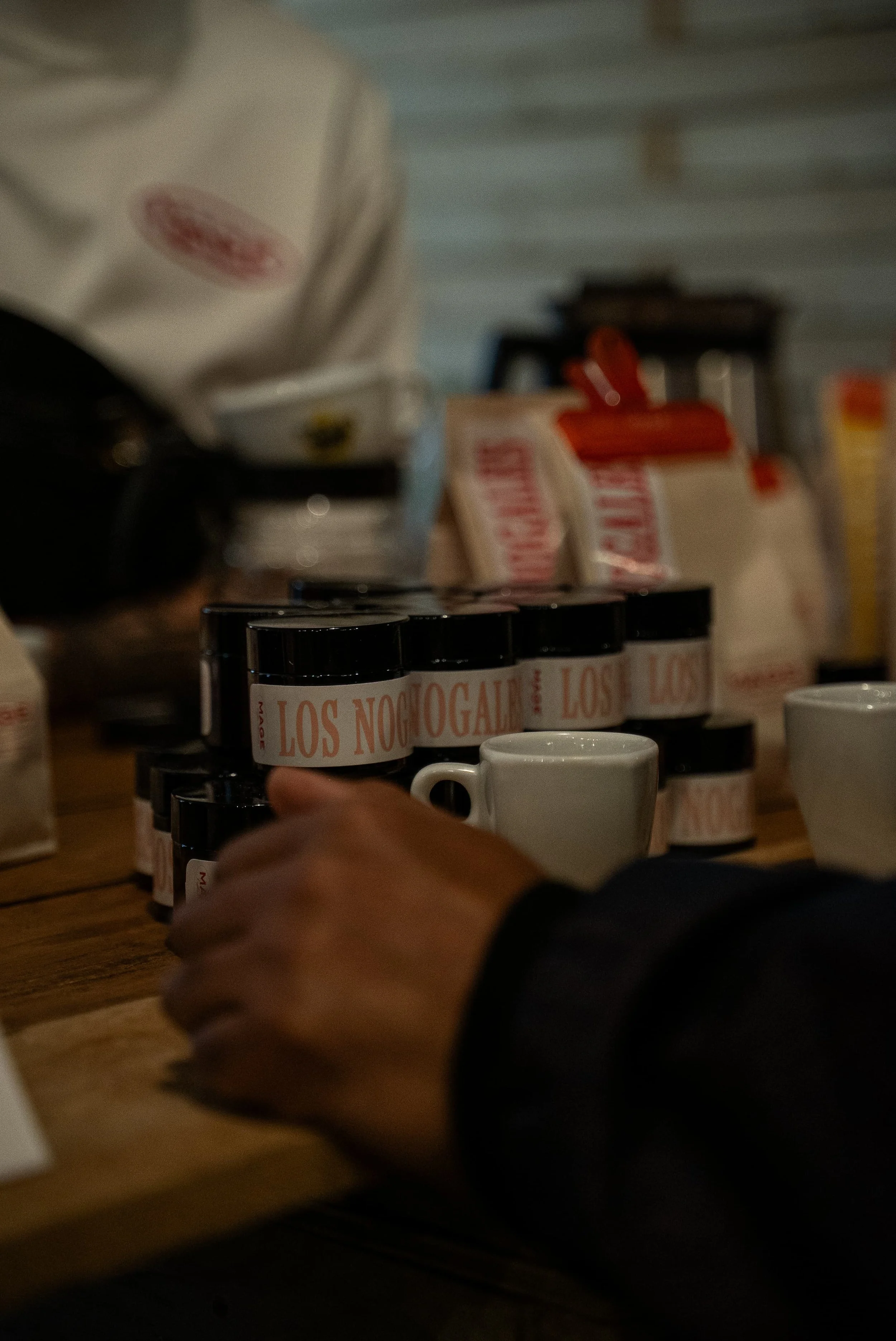 Une main d'enfant repose sur une table en bois, avec plusieurs boîtes de médicaments empilées et des tasses blanches à côté.