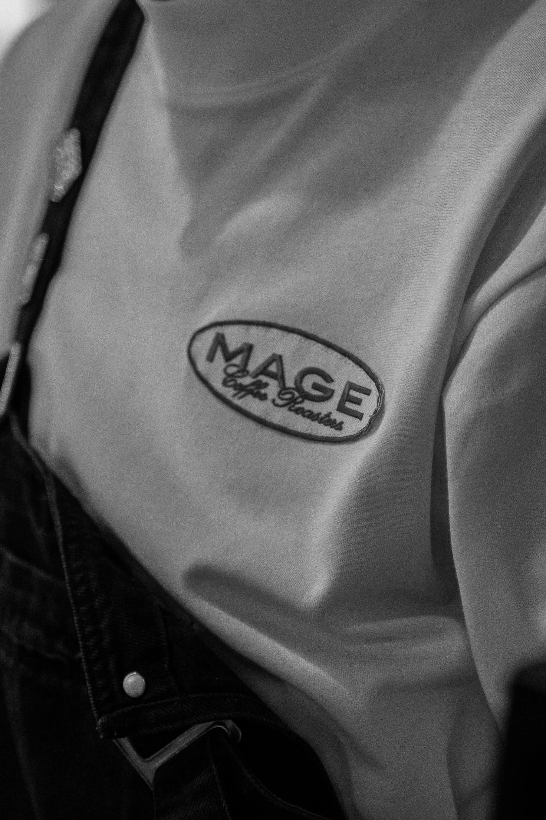 Une personne en tenues décontractées portant un T-shirt avec le logo 'MACE' et le texte 'by Holik' visible sur le devant, avec un pantalon noir.