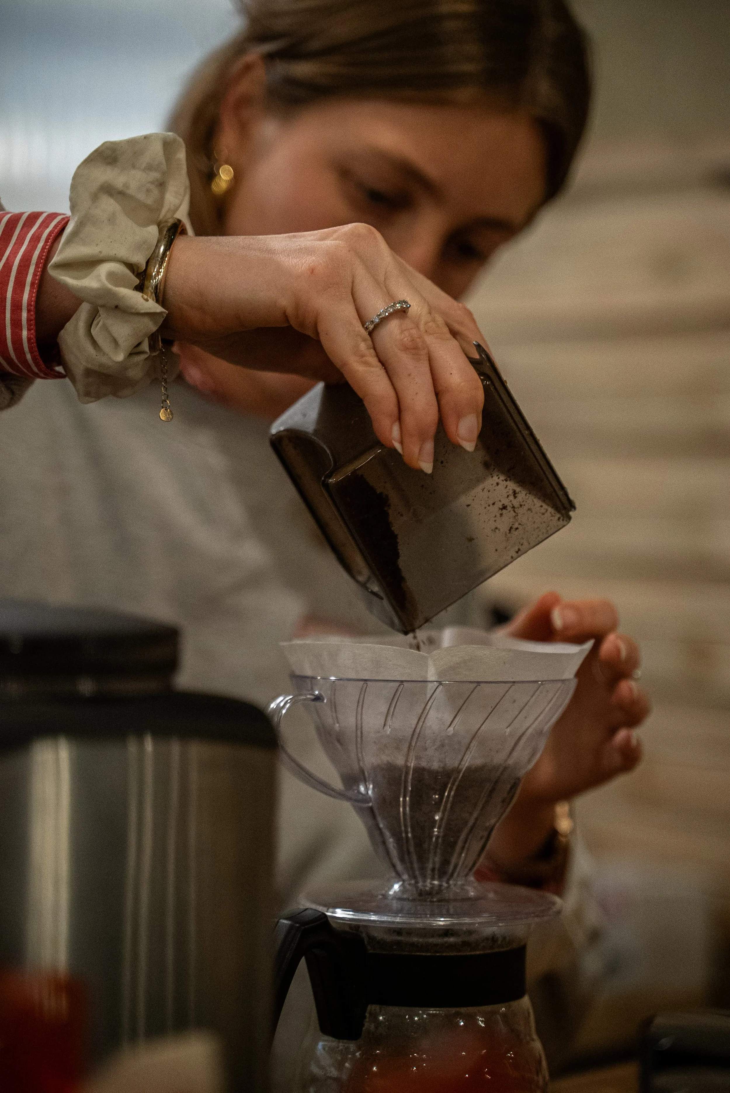 Une femme verse du café moulu dans un filtre à café placé dans une cafetière.