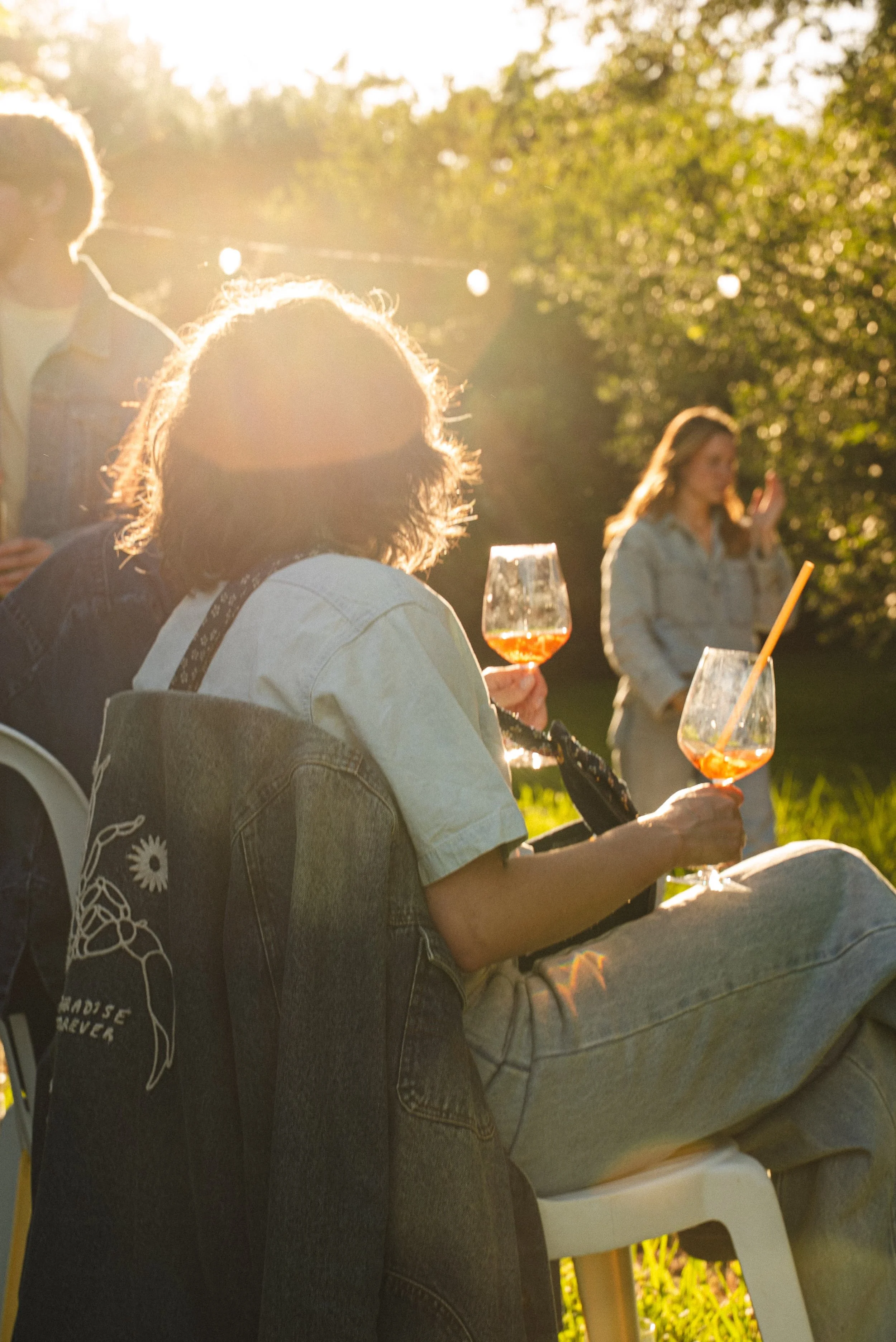 Groupe de personnes assises en extérieur, dégustant des boissons lors d'une réunion conviviale au soleil, avec des arbres en arrière-plan.