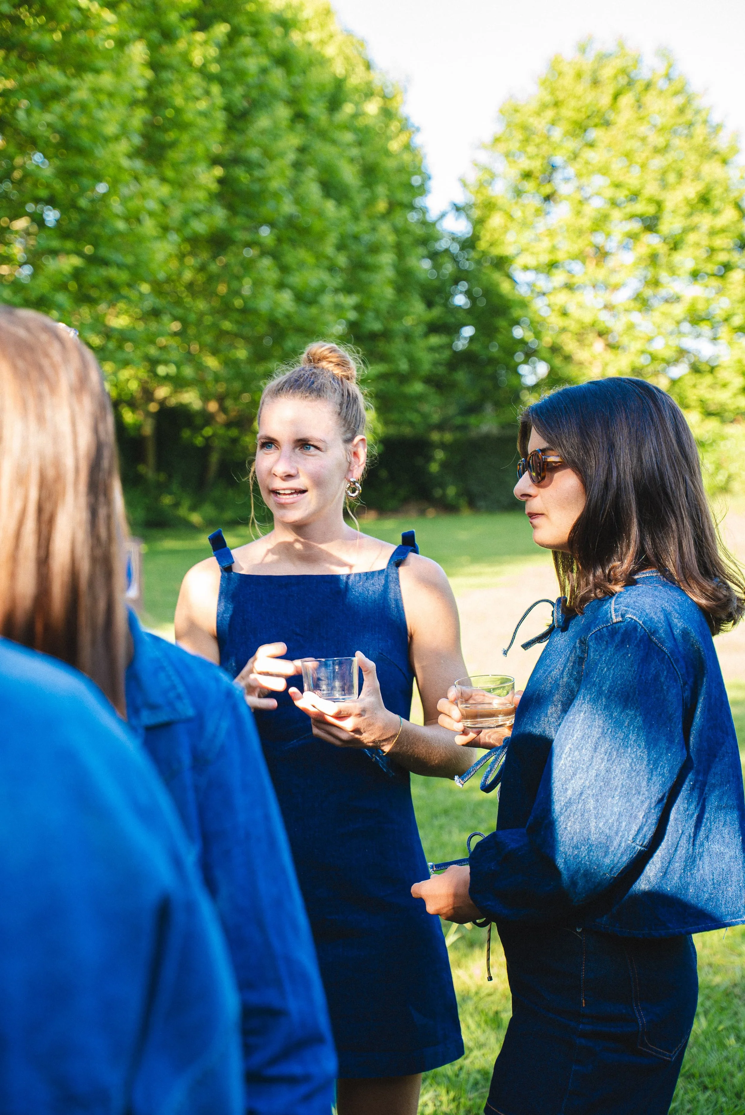 Groupe de femmes discutant lors d'un pique-nique en plein air, tenant des verres dans leurs mains, avec un arbre en arrière-plan.