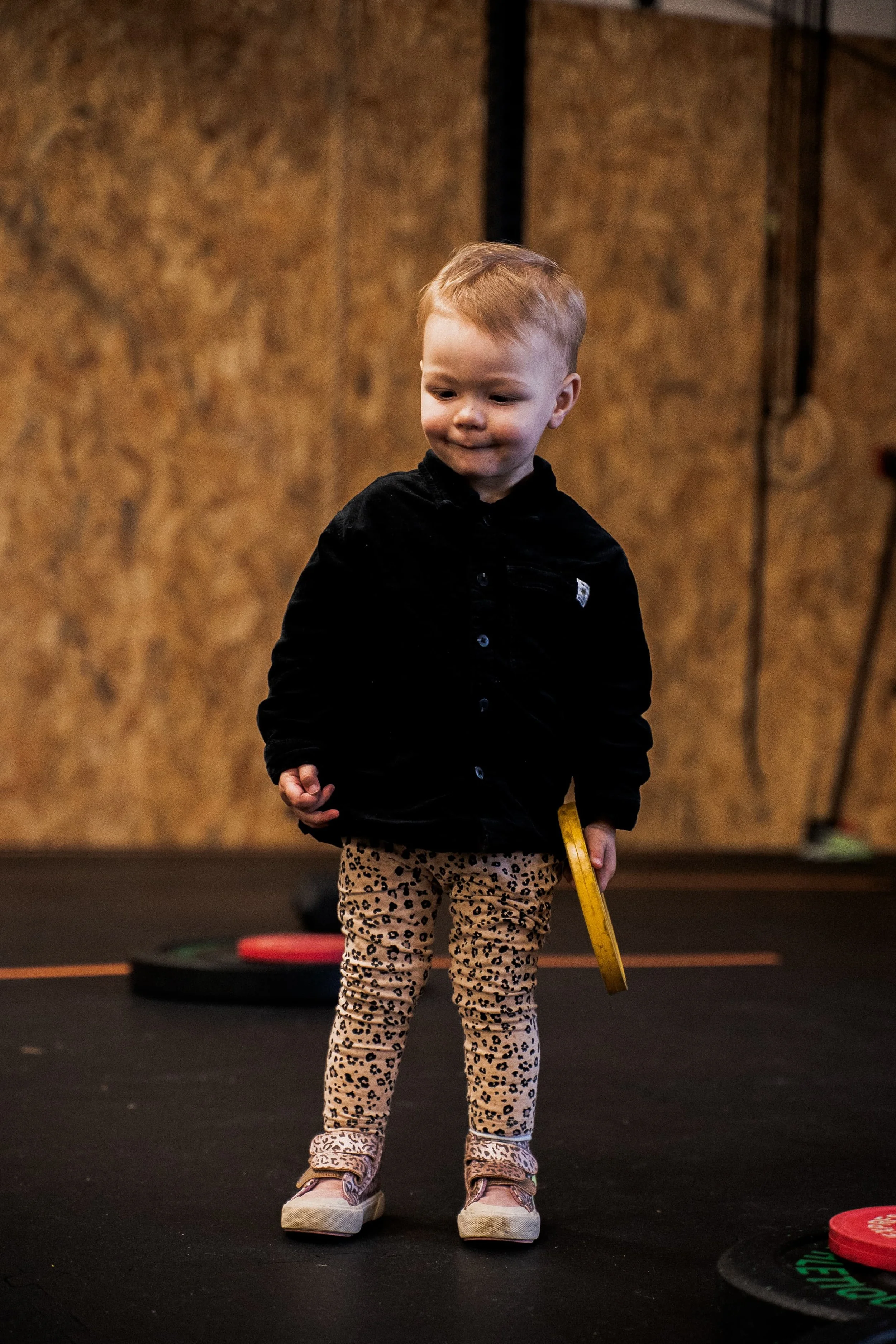 Un jeune enfant debout sur une surface noire, portant un pantalon à motif léopard, une veste noire et des chaussures roses. La scène se déroule probablement dans une salle d'amusement ou de jeu.