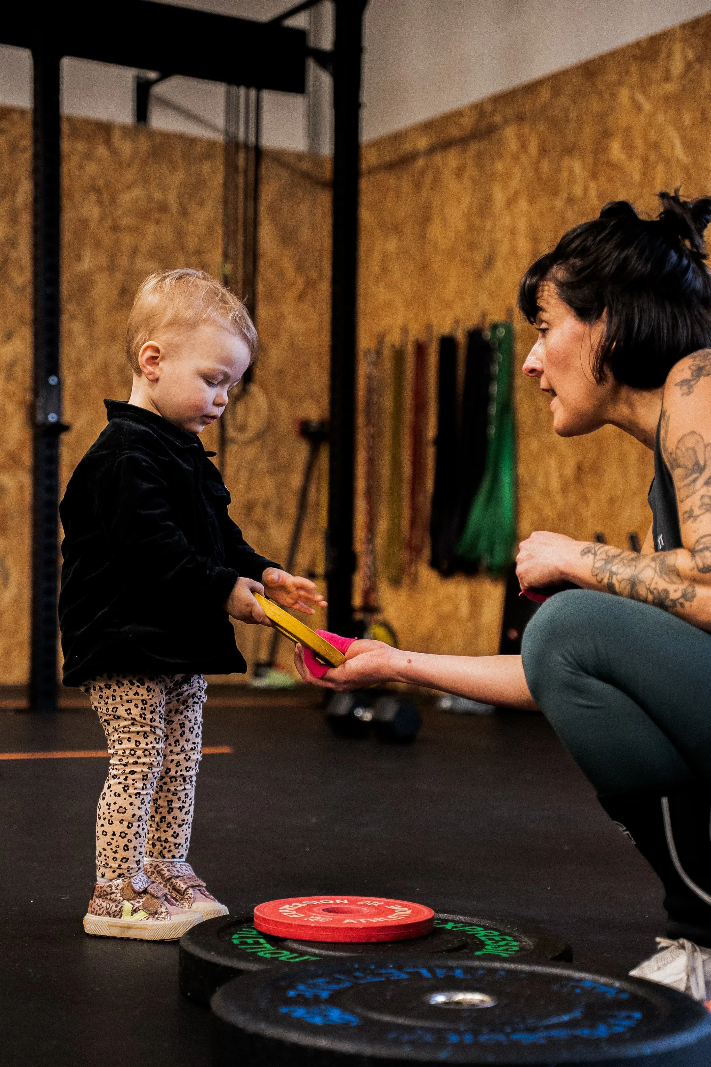 Une jeune fille avec des vêtements à motif léopard reçoit un trophée ou une récompense d'une entraîneuse dans une salle d'entraînement ou de musculation, avec des haltères et des poids en arrière-plan.
