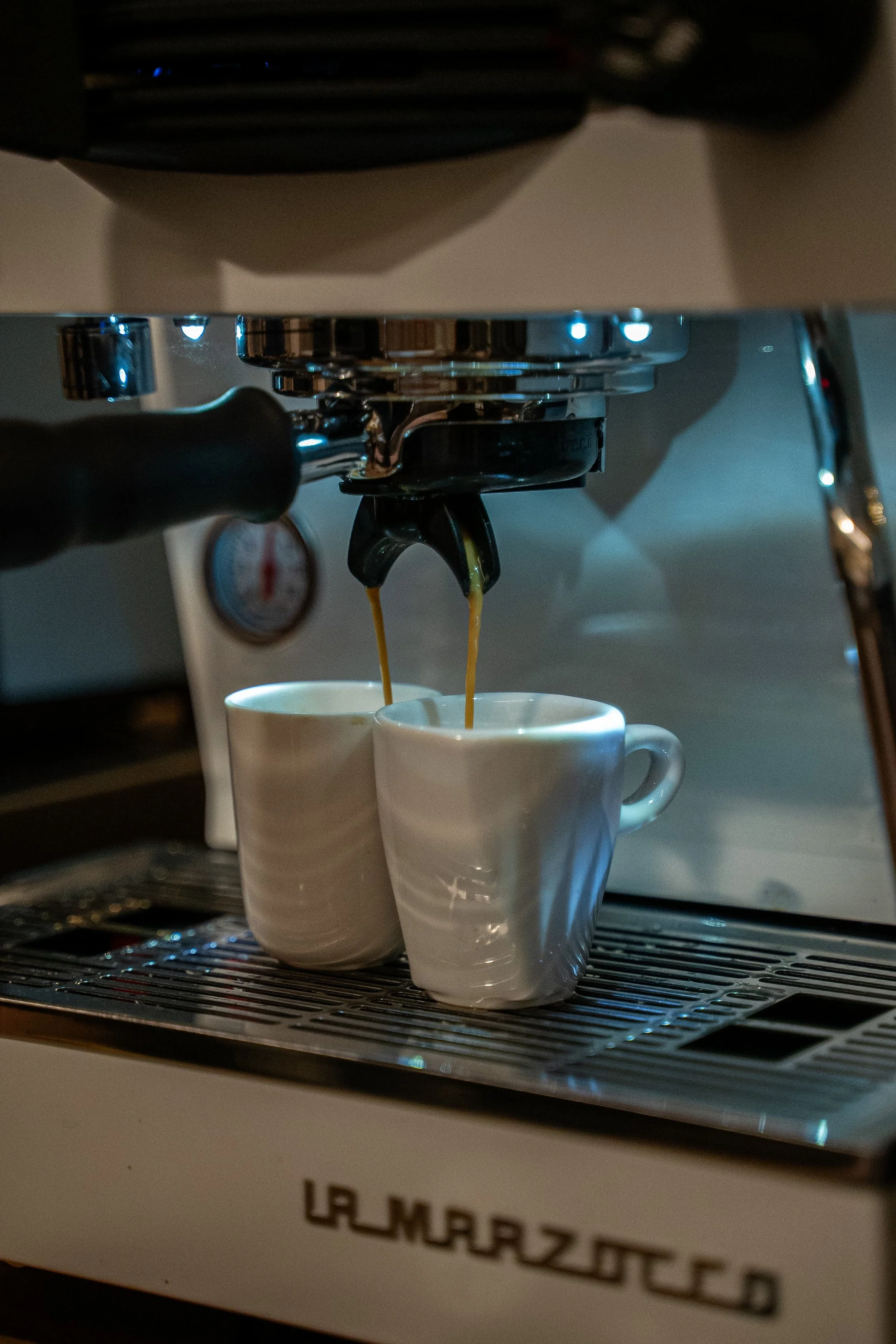 Une machine à café grindant du café dans deux tasses blanches.