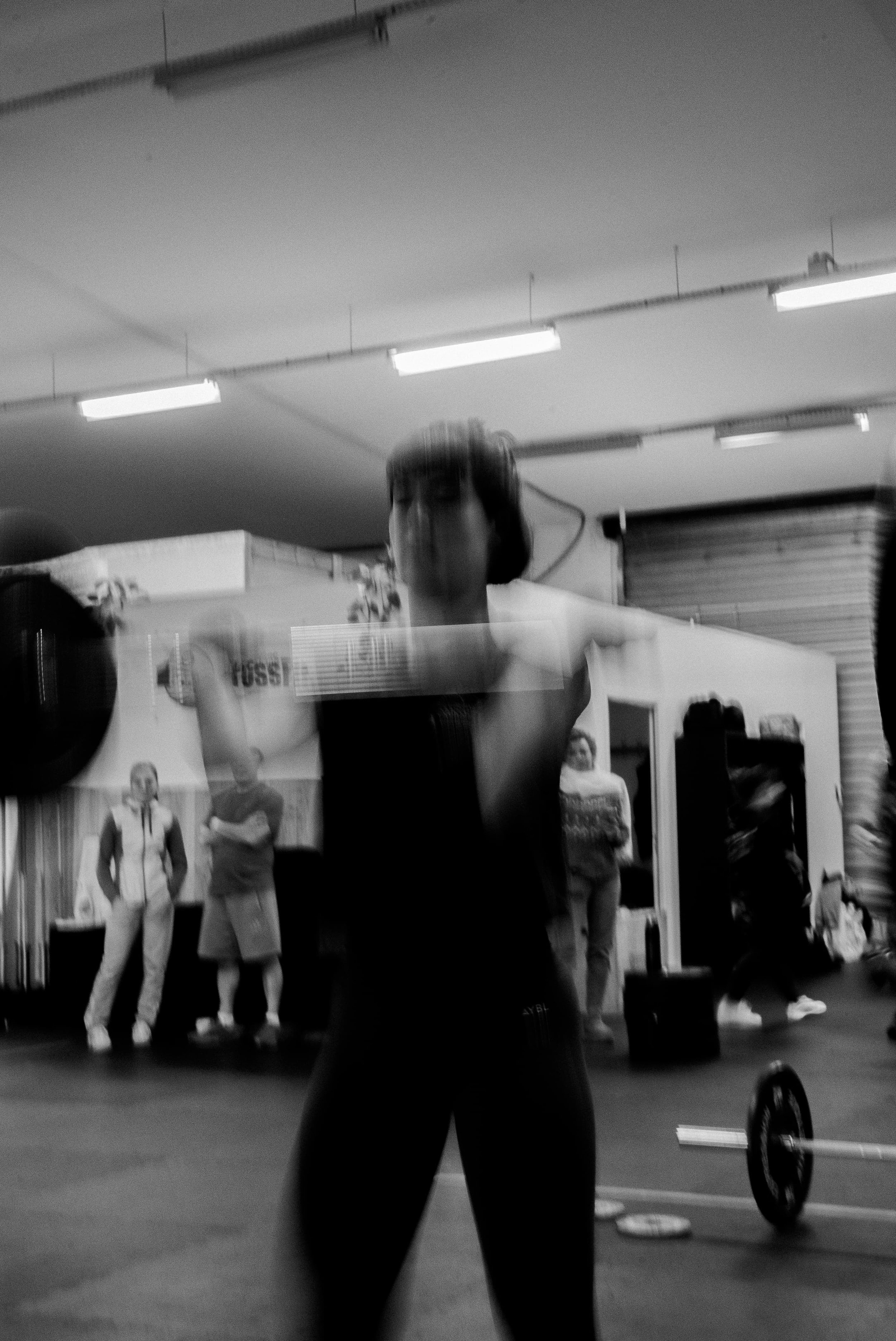Une personne en train de faire de la musculation dans une salle de sport, avec d'autres personnes en arrière-plan et des équipements de fitness