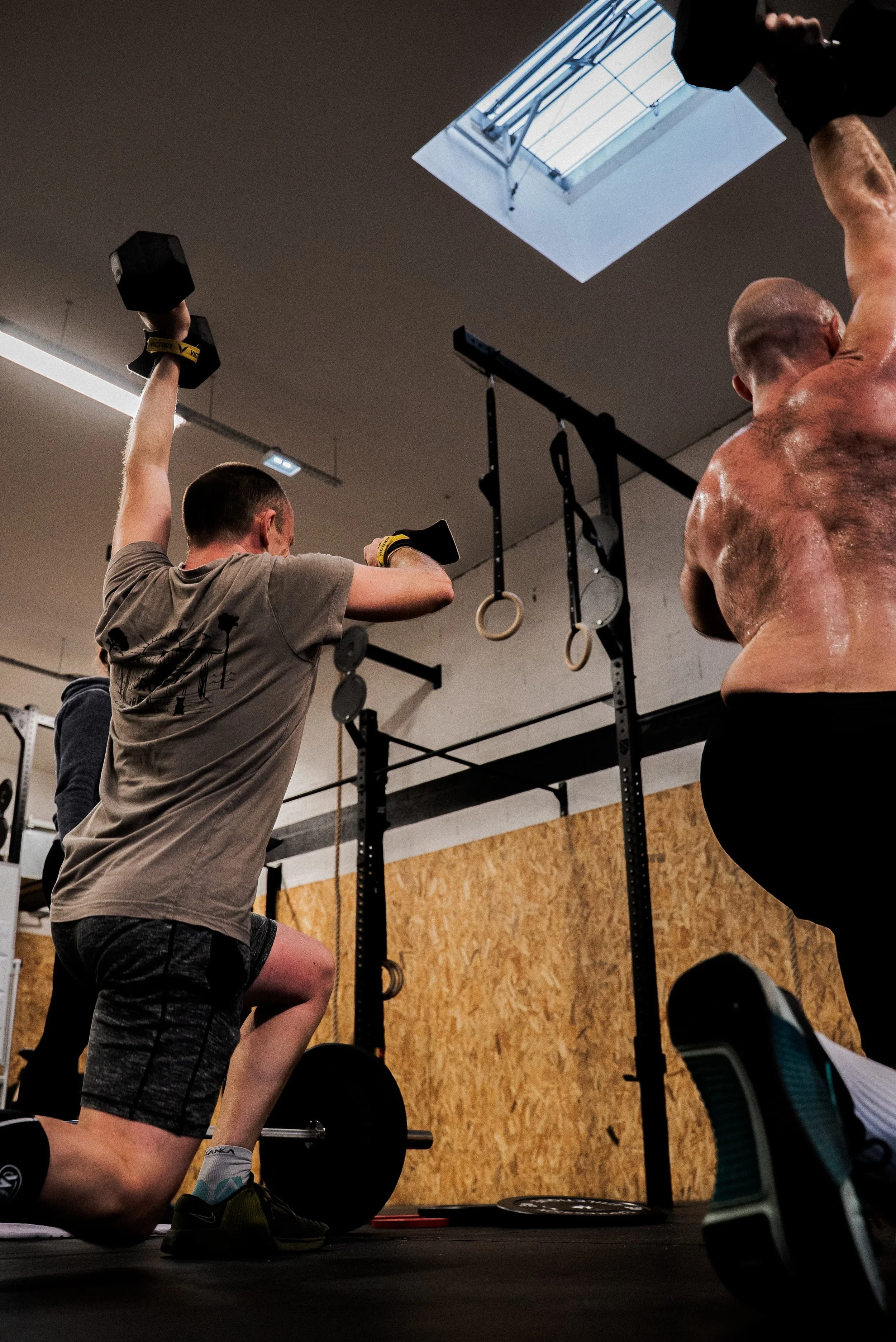 Une personne effectue un squat avec une haltère dans une salle de sport, avec un plafond connu pour ses fenêtres de lumière naturelle.