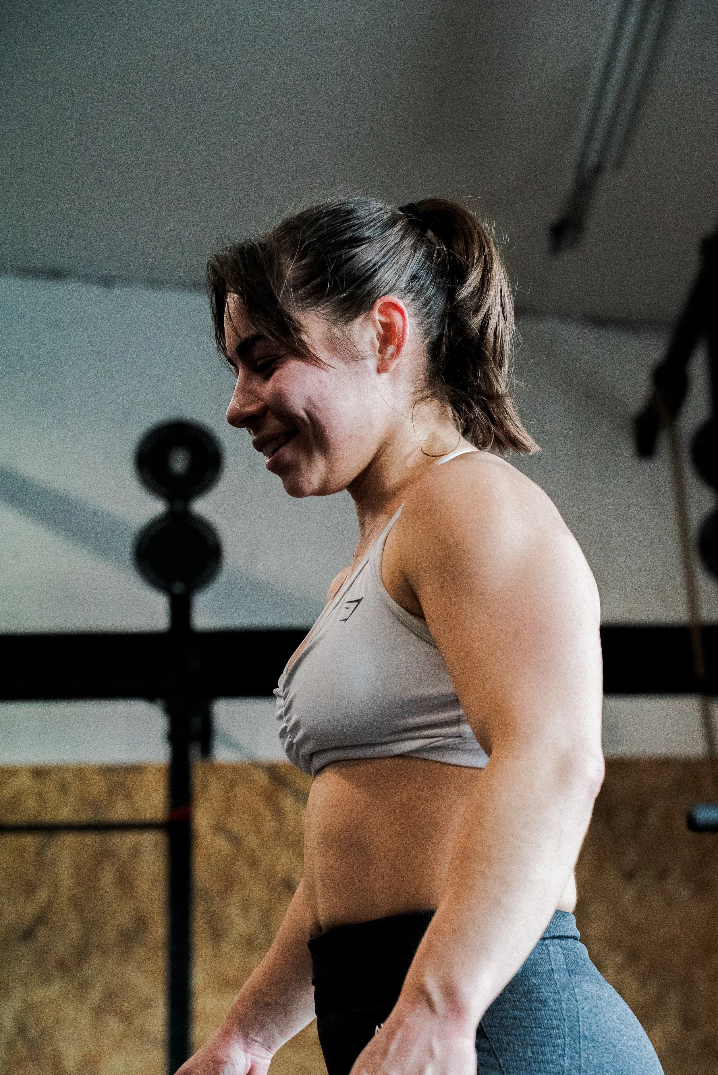 Une femme souriante en tenue de sport dans une salle de sport, en train de faire une activité physique.