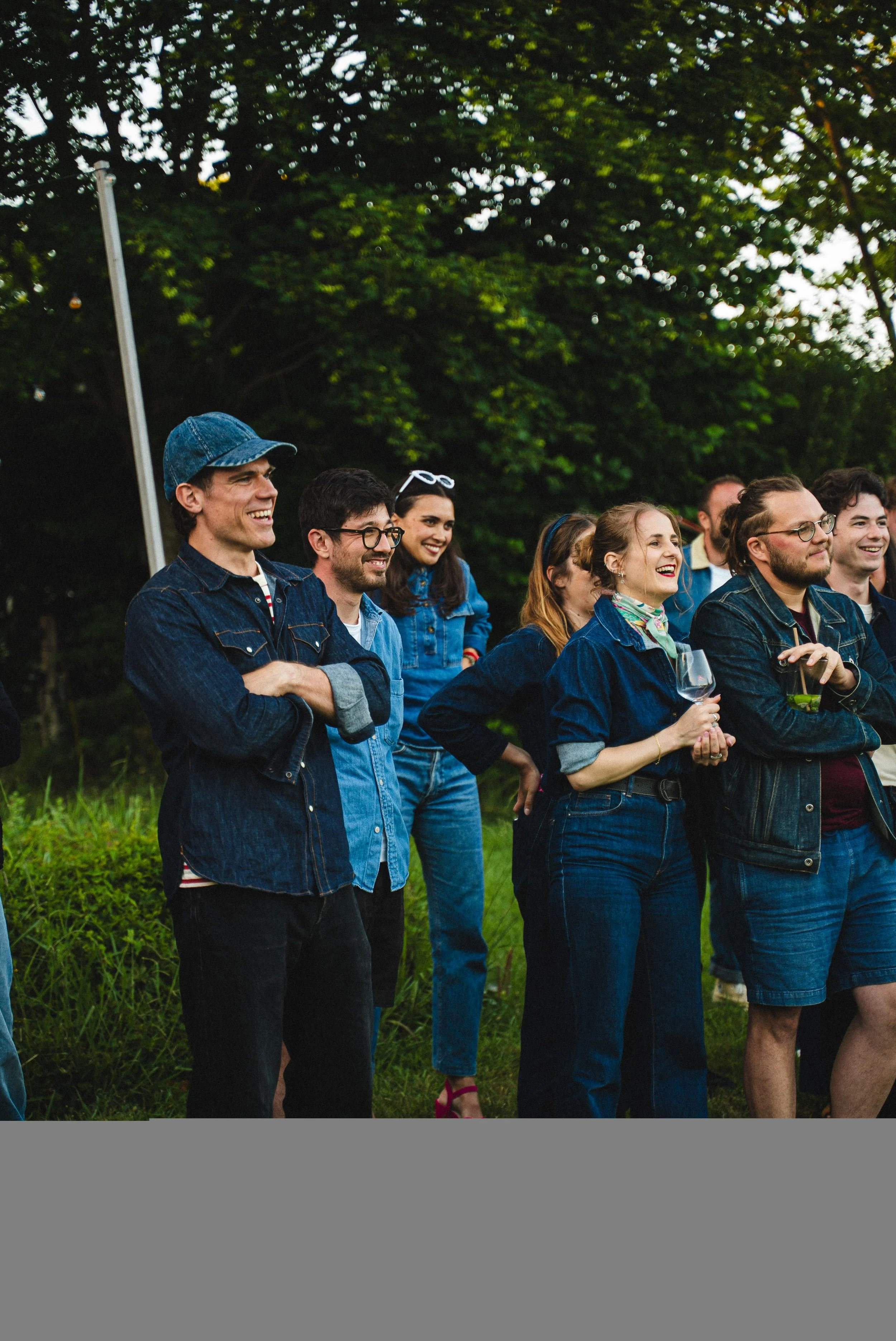 Groupe de personnes souriantes, habillées en jeans, en réunion en plein air dans un parc verdoyant.