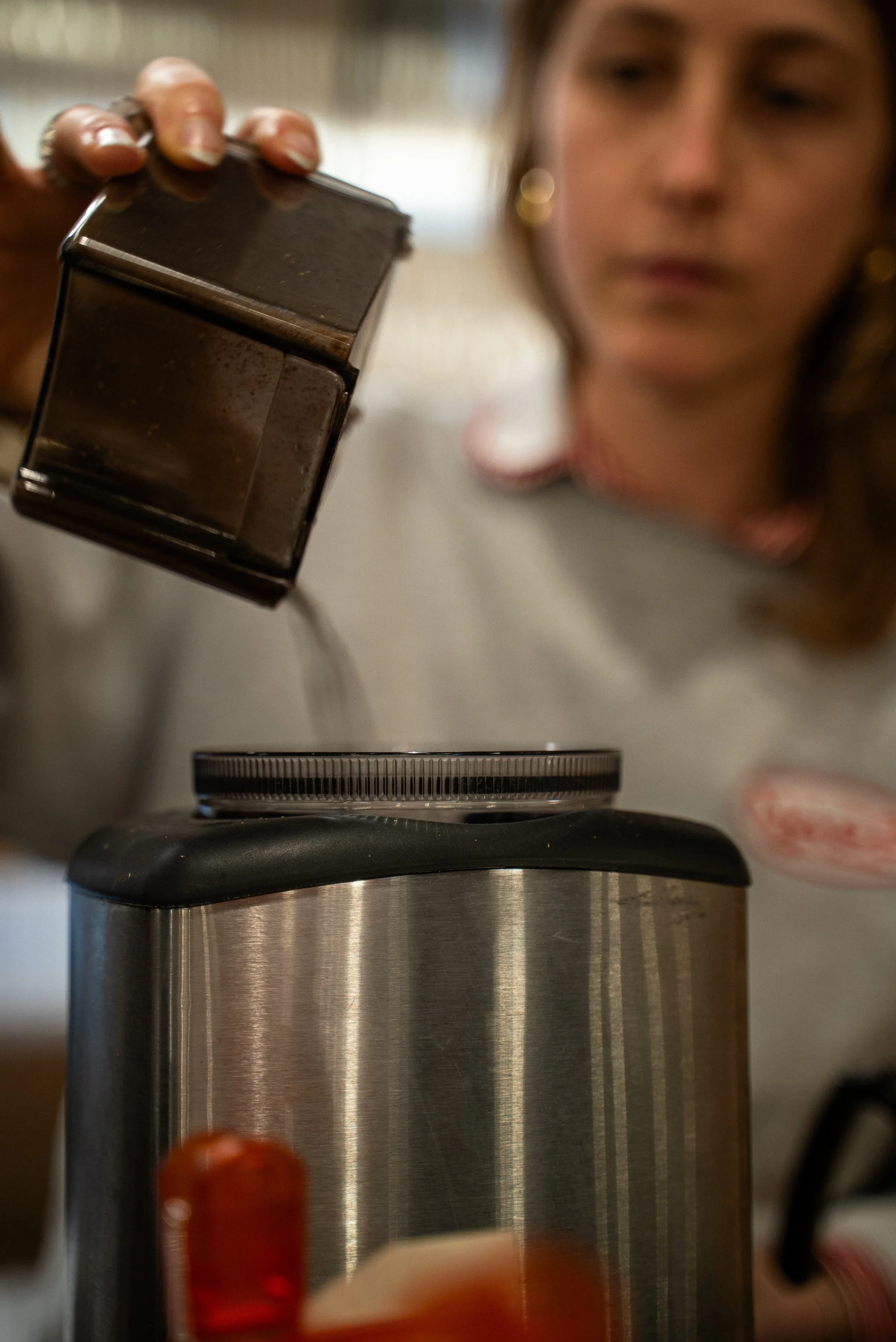 Une femme semble vérifier un device électronique ou un objet dans un environnement domestique ou de travail, avec un thermos en acier inoxydable visible au premier plan.