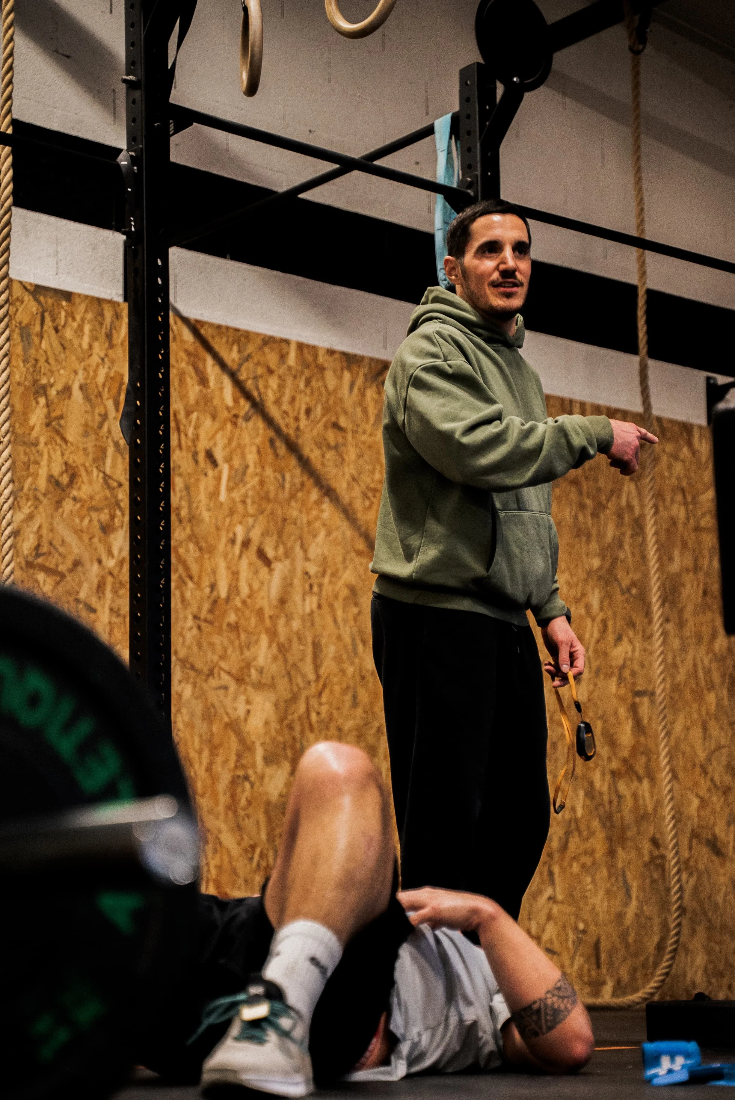 Un entraîneur ou un instructeur s'adresse à un groupe dans une salle de sport ou une salle de musculation, avec des équipements d'exercice visibles en arrière-plan.