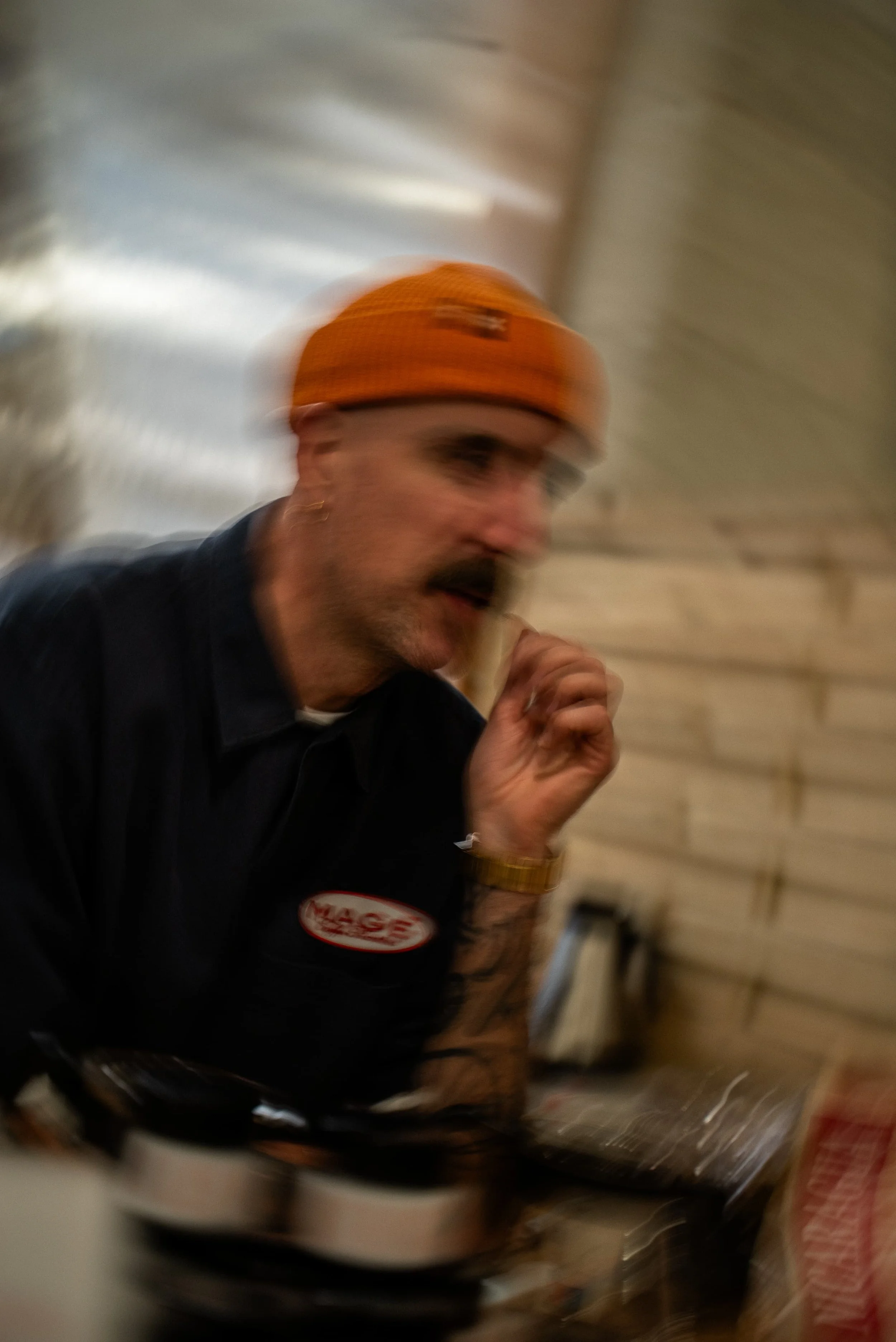 Une personne portant un casque orange et une veste noire est en mouvement dans une pièce, avec un fond flou et des meubles visibles.