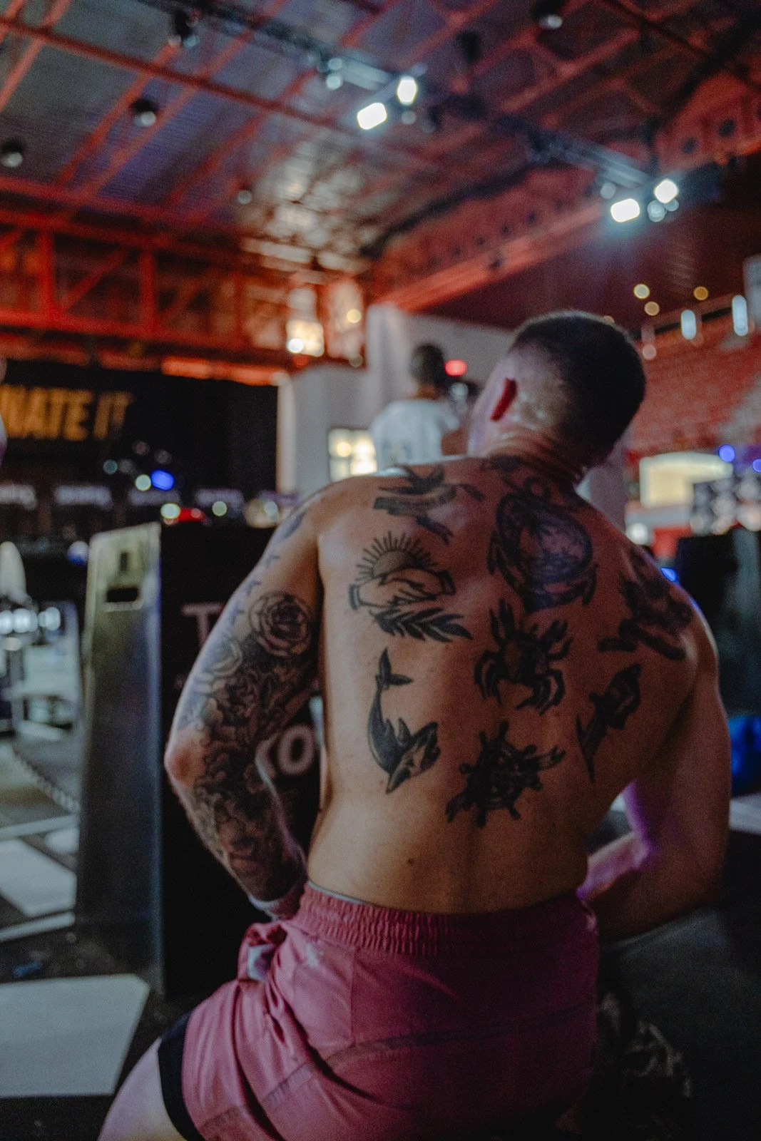 Athlète tatoué torse nu lors d'un événement sportif en salle avec plafond métallique rouge — photographe fitness Voar by Tim