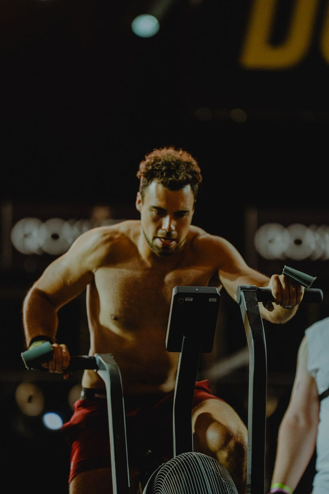 Homme torse nu s'entraînant sur vélo elliptique dans une salle de sport CrossFit — photographe fitness Voar by Tim