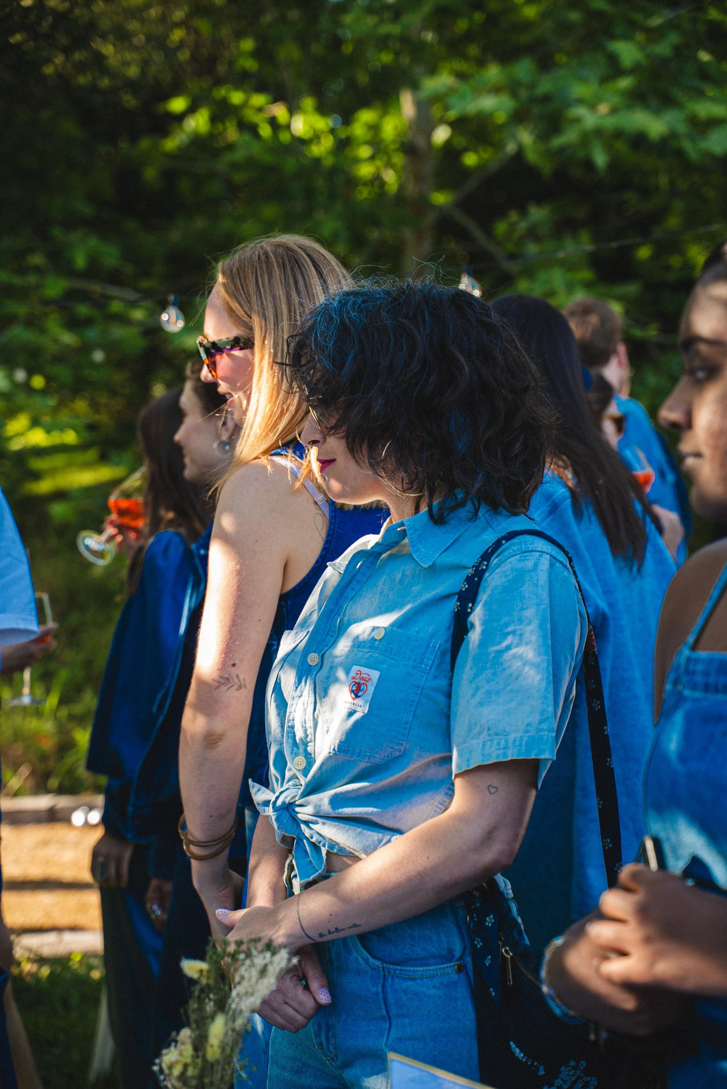 Groupe de personnes assises en extérieur sous un arbre, participant à une activité ou un événement lors d'une journée ensoleillée.
