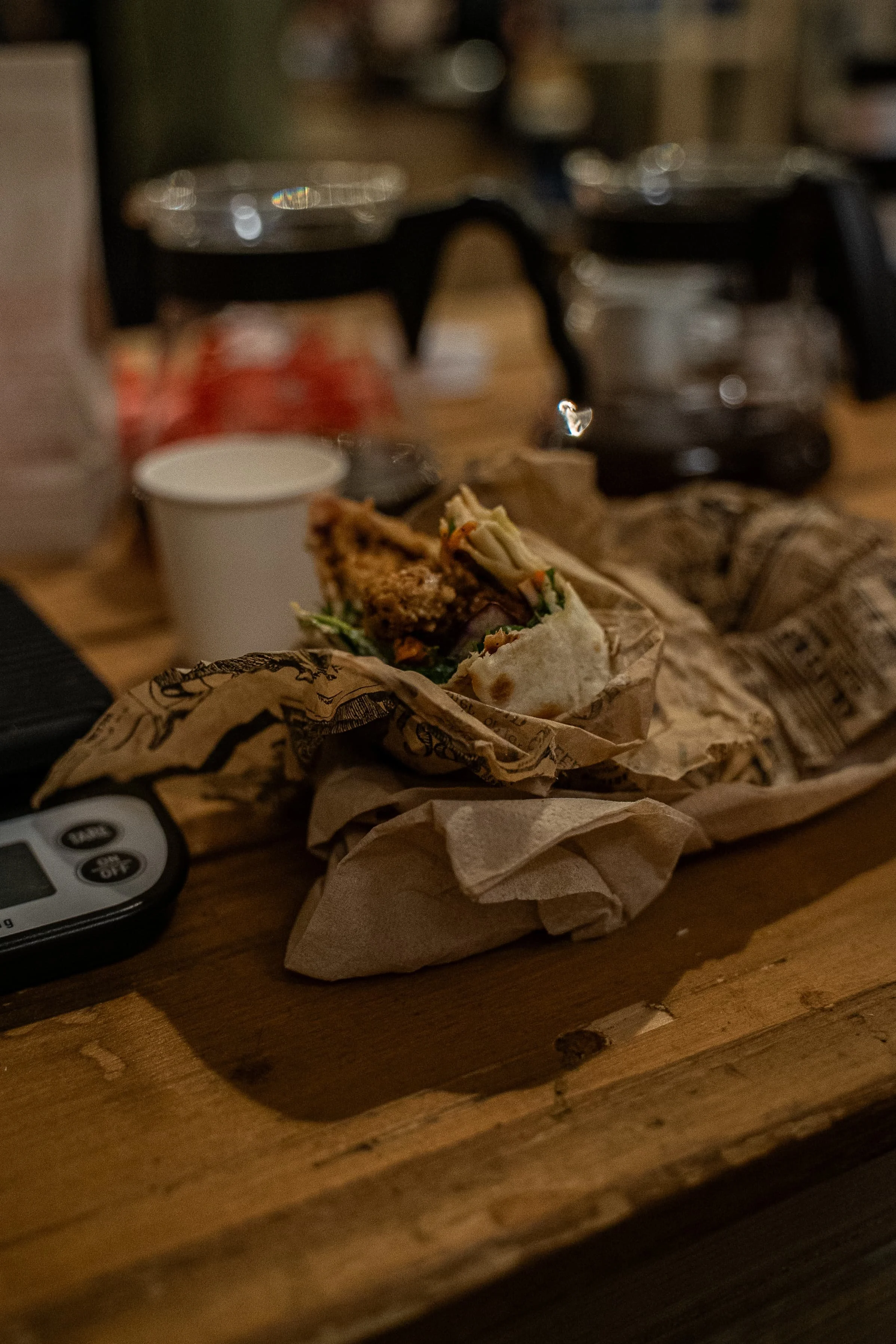 Un sandwich dans un papier représentant un journal, placé sur une table en bois.