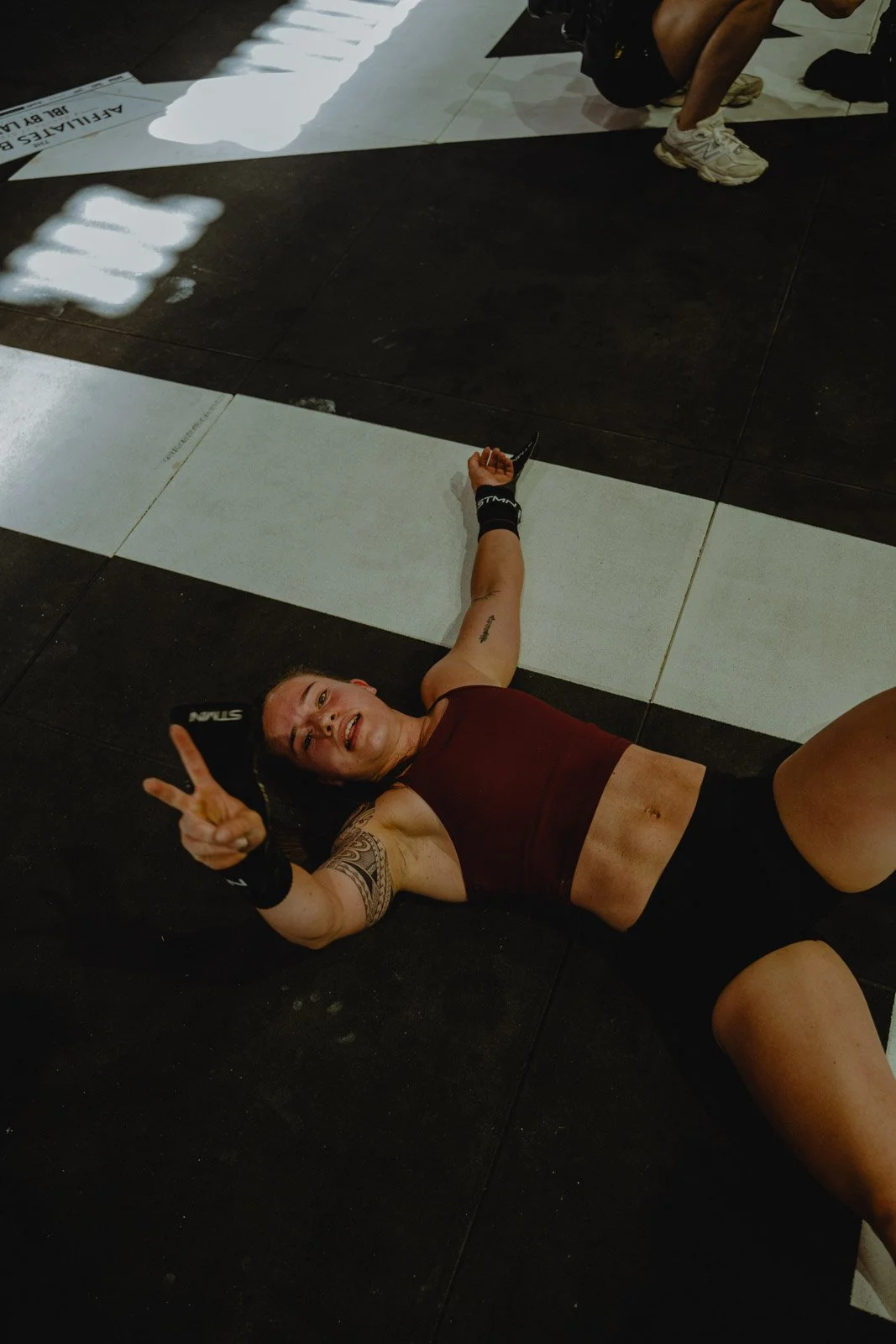 Femme tatouée avec gants d'entraînement allongée au sol faisant signe de paix après séance CrossFit à Bordeaux — photographe CrossFit Voar by Tim