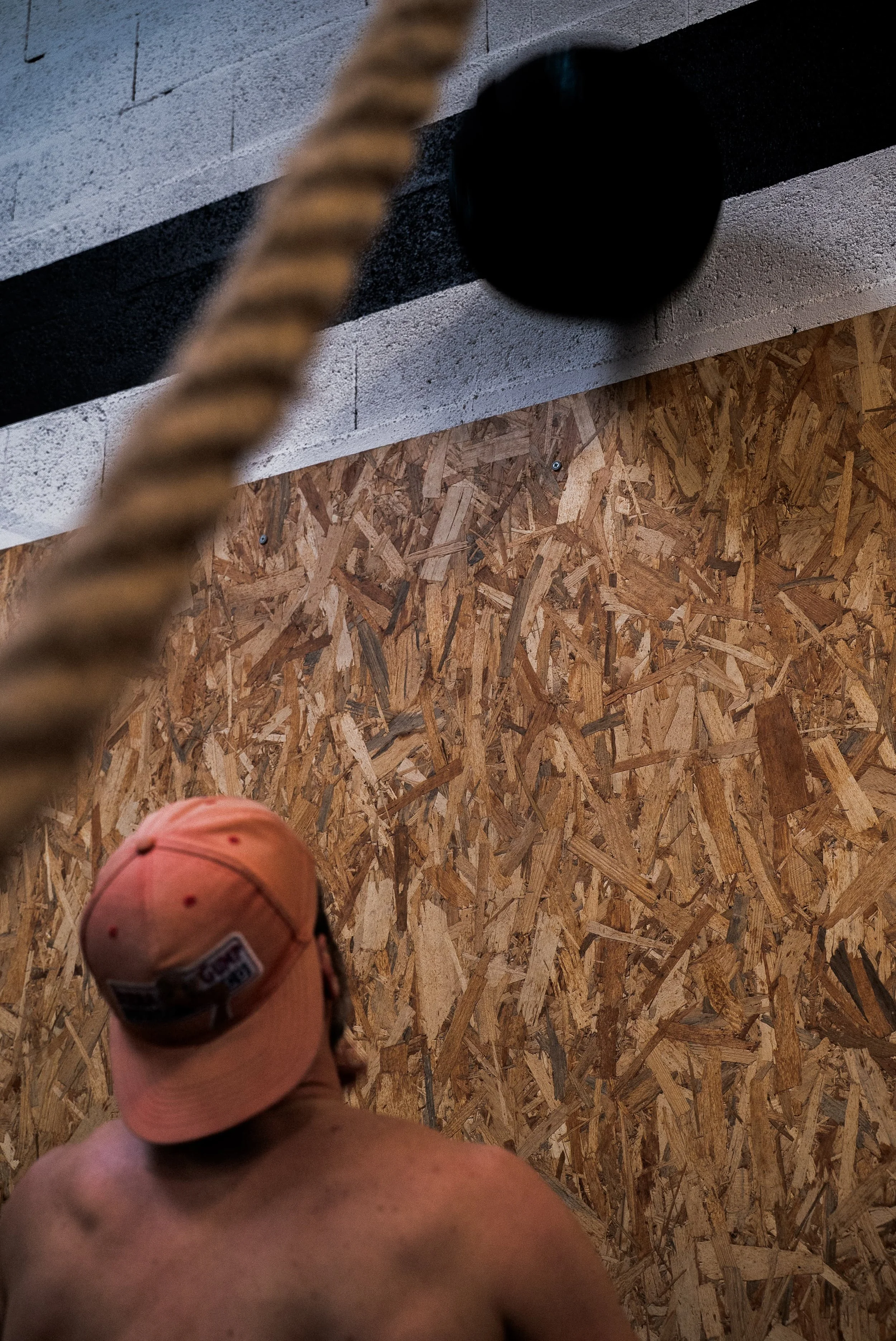 Personne portant une casquette beige et un casque audio, vue de dos, dans un espace avec un mur en bois aggloméré.