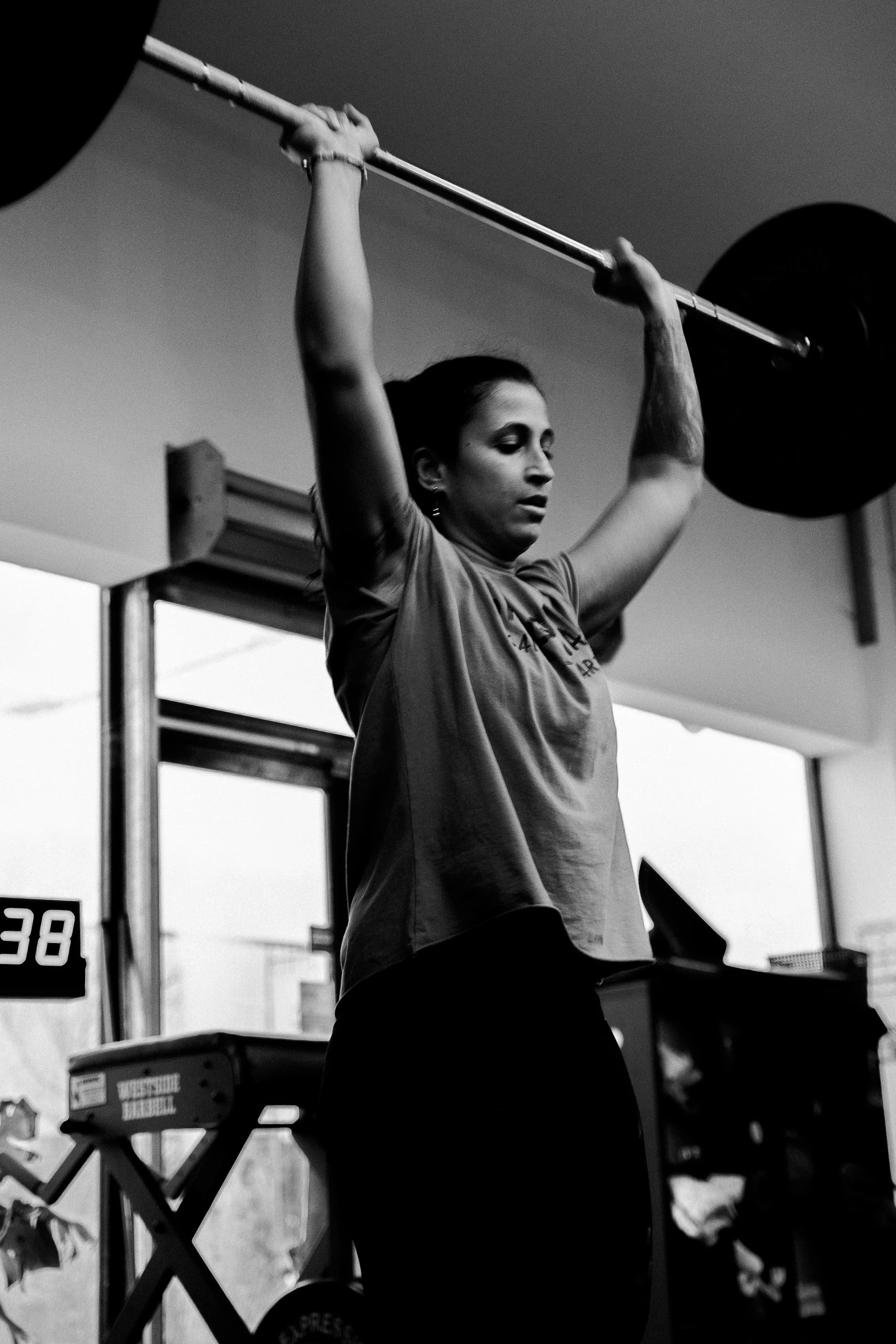 Une femme soulève une barre de musculation lors d'une séance d'entraînement, vue en contre-plongée en noir et blanc.