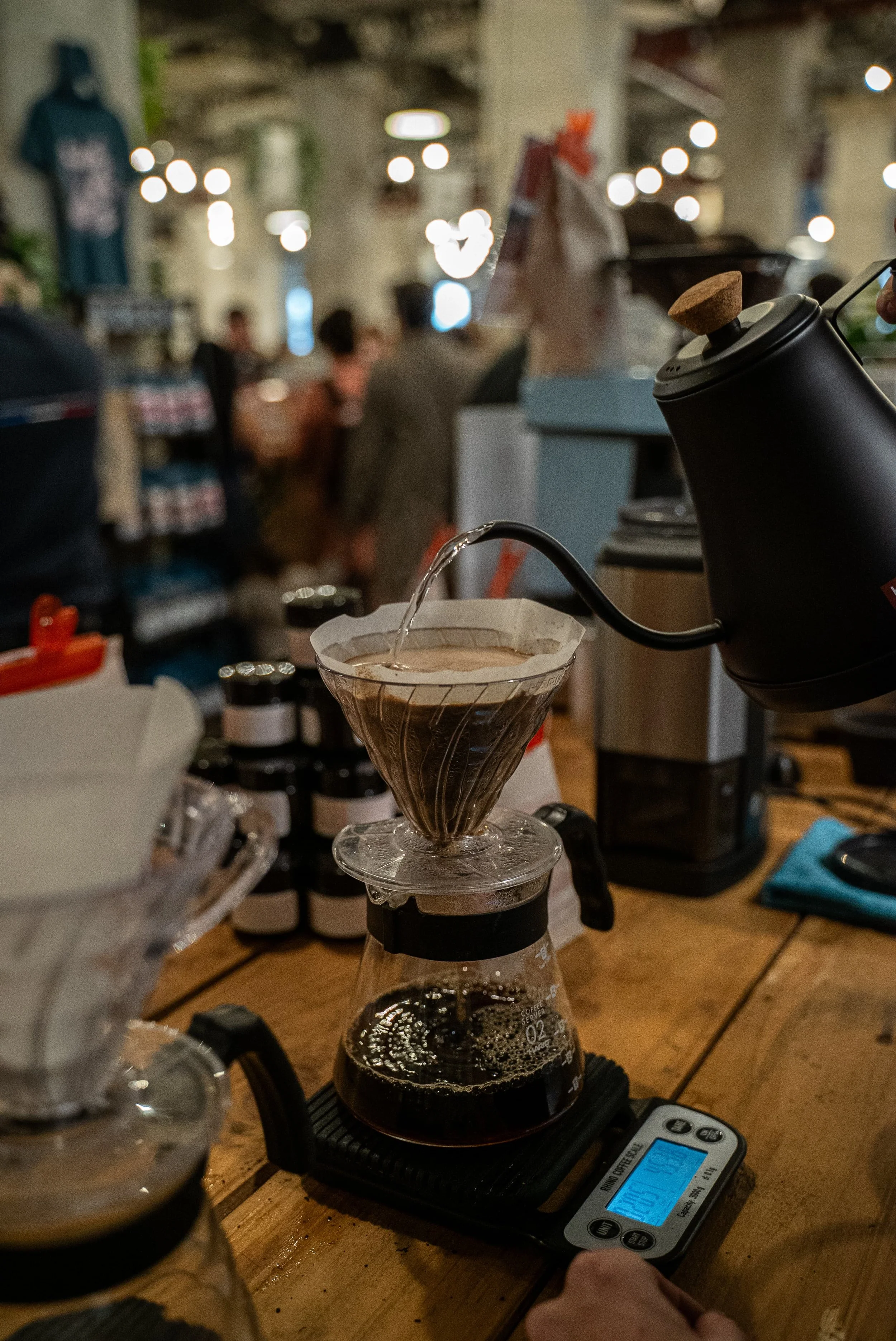 Préparation du café avec une cafetière Chemex, l'eau chaude est versée sur le café moulu dans le filtre, posé sur une balance numérique sur une table en bois dans un café ou un espace de travail 