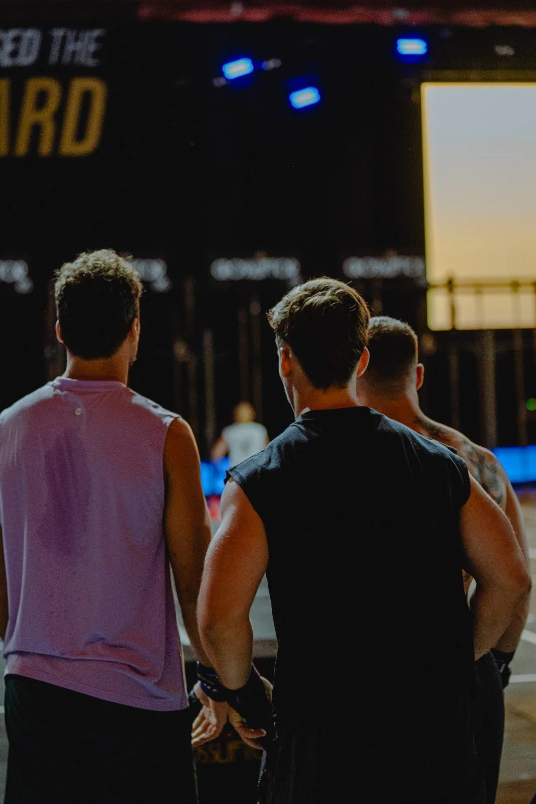 Trois jeunes hommes regardant un grand écran lors d'un événement sportif CrossFit — photographe événement Voar by Tim
