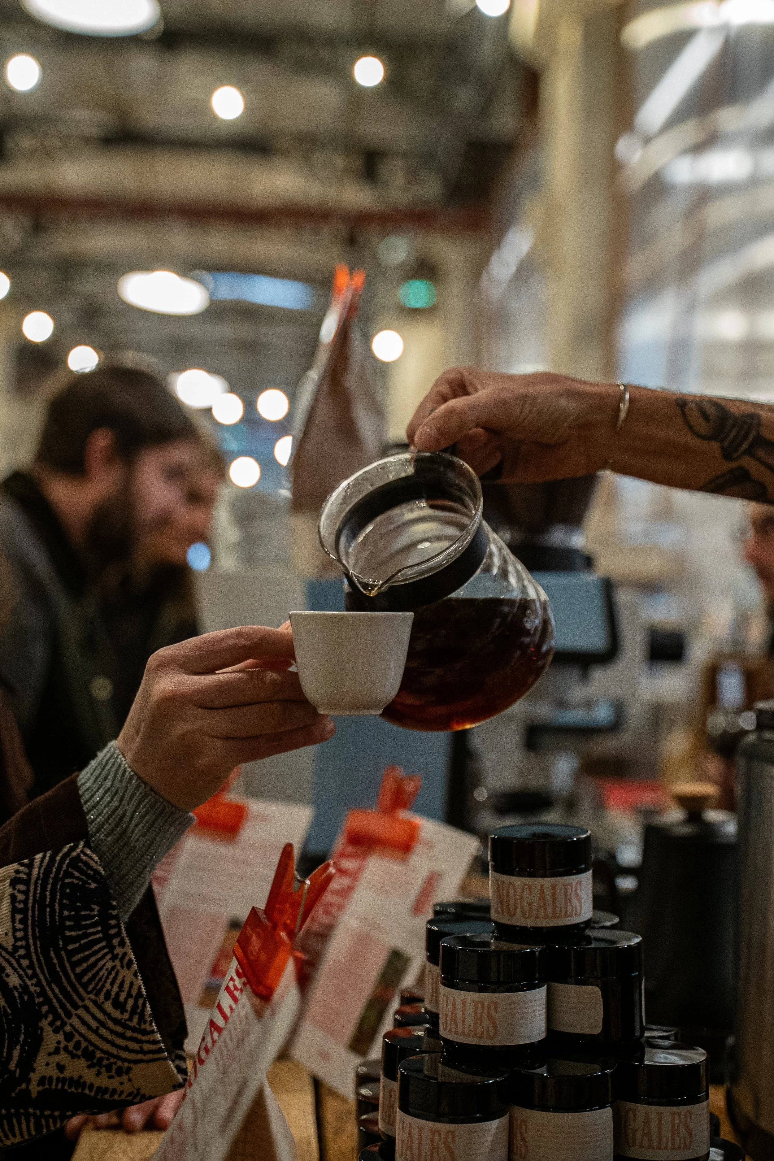 Personne versant du café dans une tasse dans un environnement intérieur, avec des bouteilles de sauces sur un étagère.
