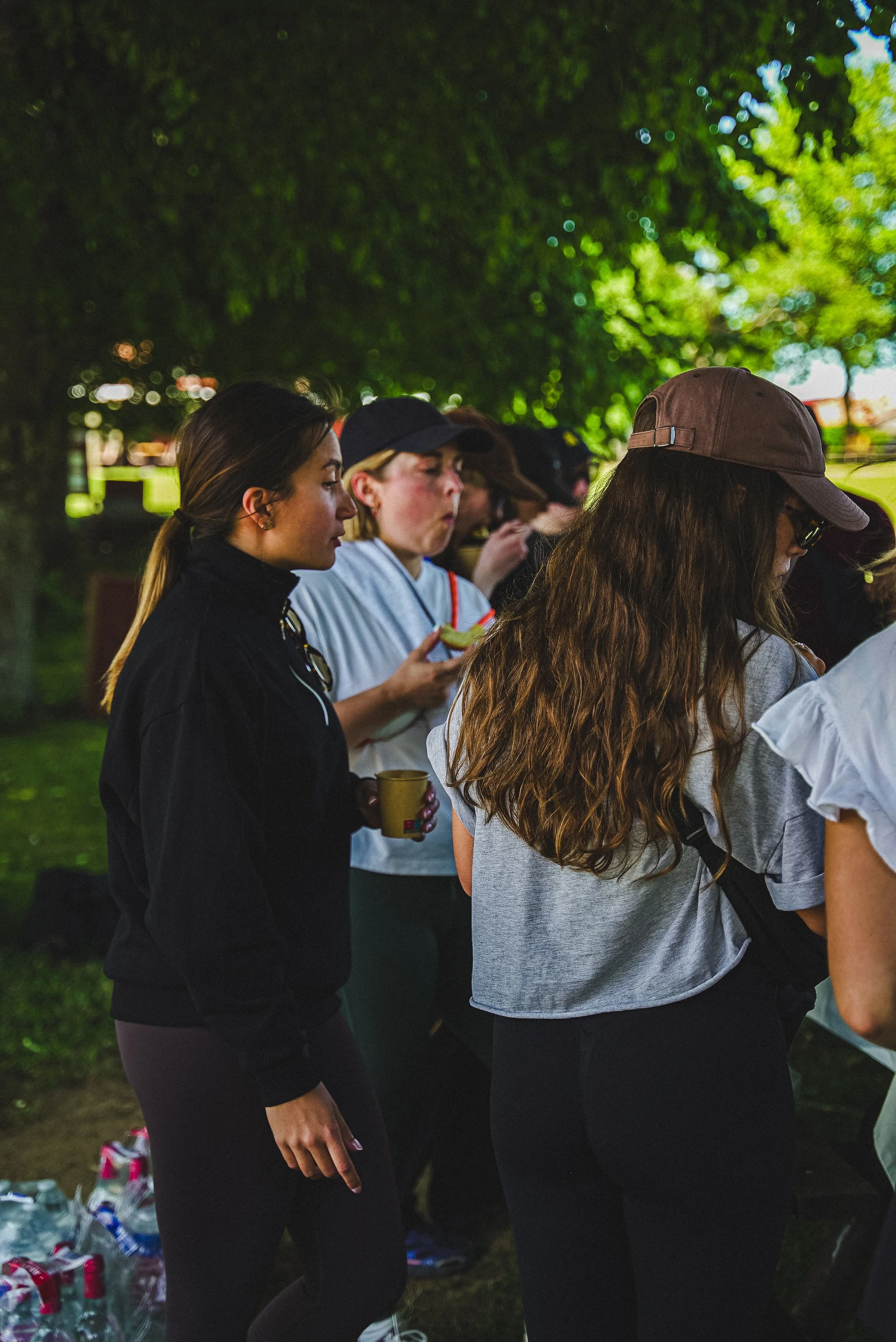 Un groupe de jeunes femmes qui font la queue lors d'une sortie en plein air, probablement une fête ou un rassemblement, sous un arbre en pleine journée.