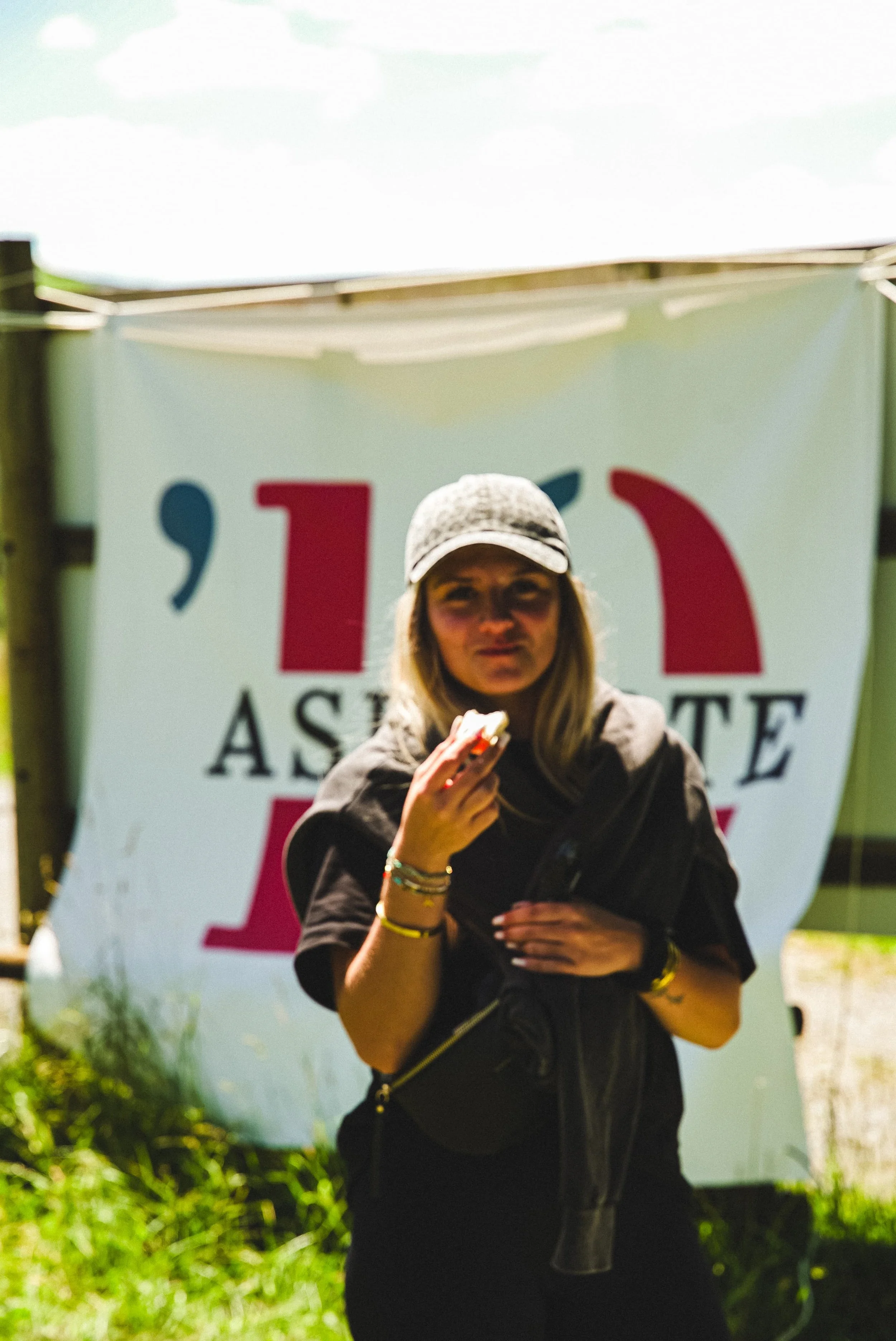Une femme portant un casque et un manteau noir, faisant un signe de paix avec la main devant un panneau avec un texte partiel 'ASSE'.