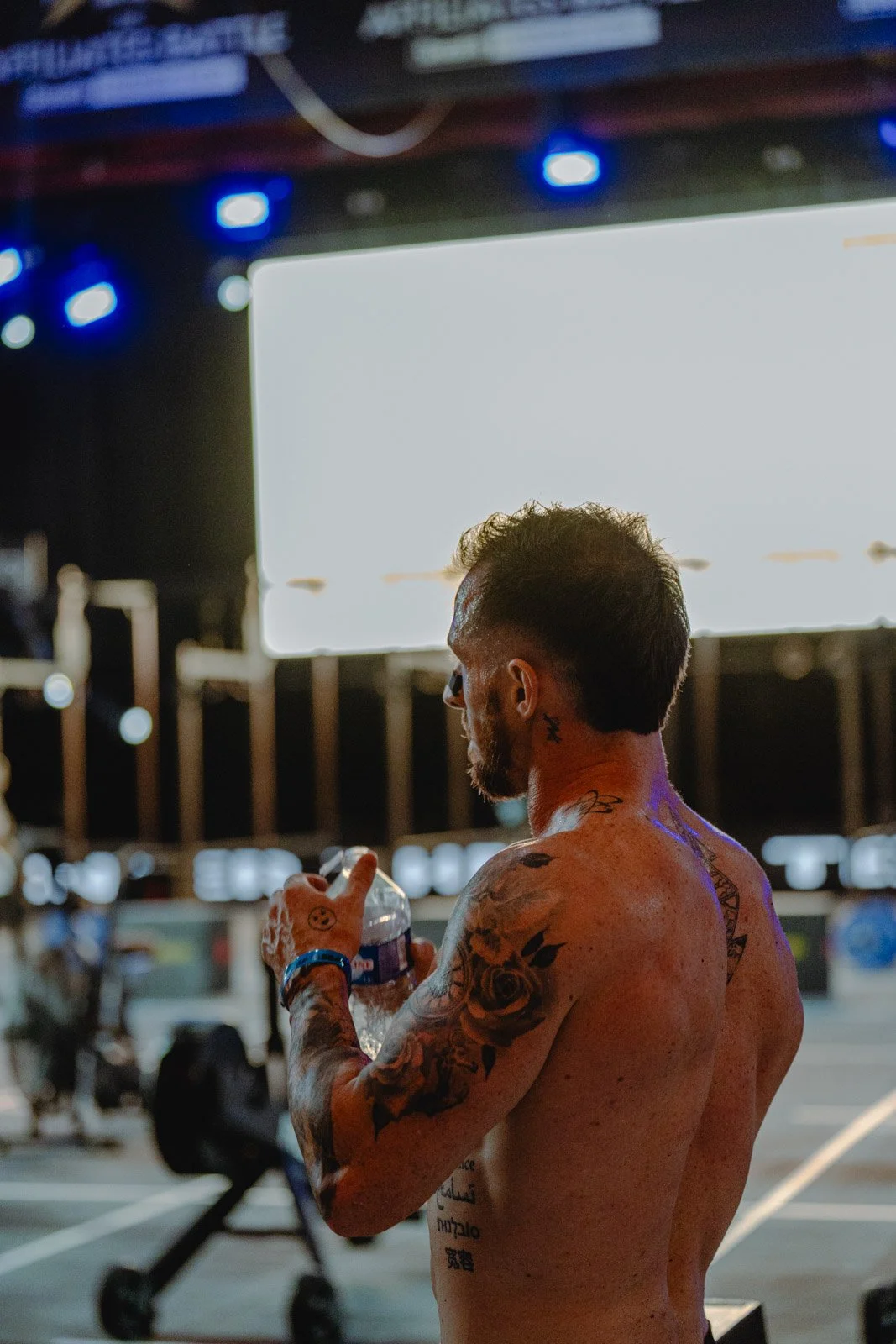 Homme torse nu avec tatouages tenant une bouteille d'eau lors d'une compétition CrossFit — photographe fitness Voar by Tim