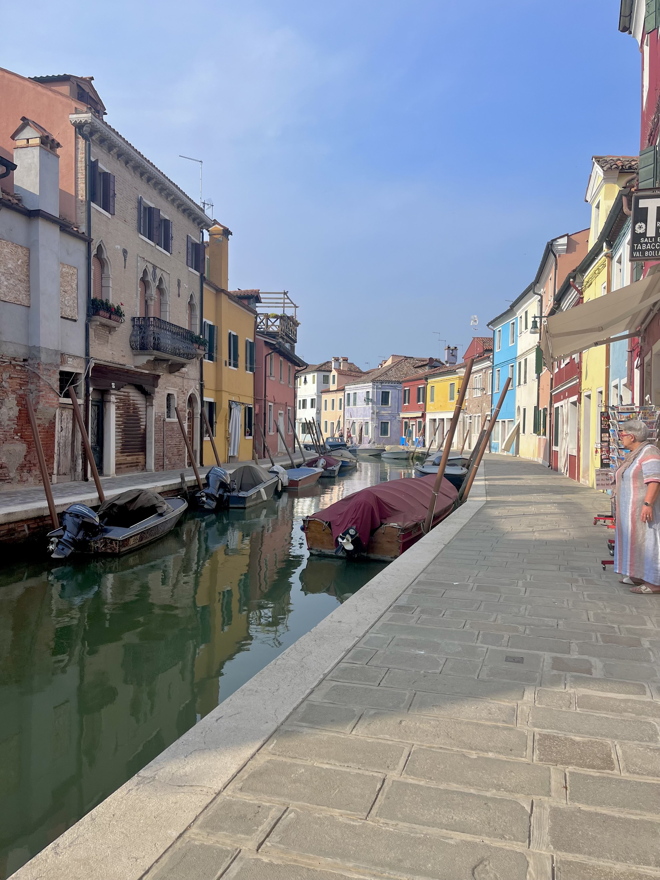 Colorful buildings lining a canal with boats and a stone walkway on a clear day.
