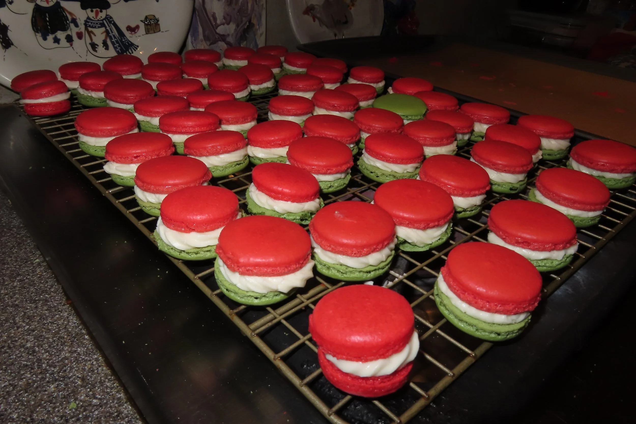 Red, green, and white macarons with a cream filling on a cooling rack.