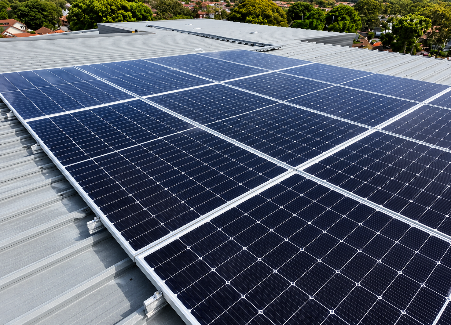 Solar panels installed on a gray rooftop with a residential neighborhood and green trees in the background.