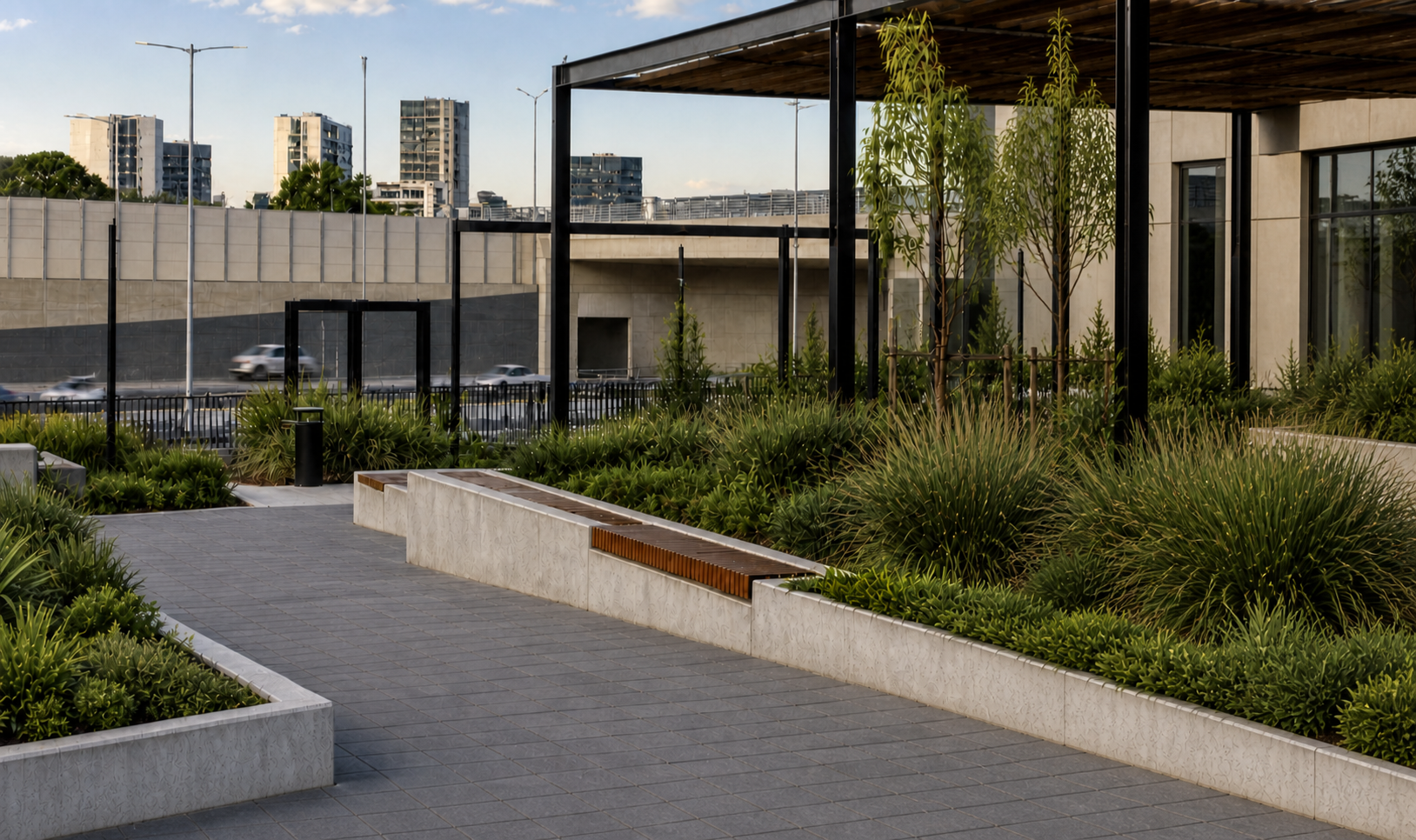 Urban outdoor scene featuring modern landscaping with green plants, trees, a paved walkway, and a building with large glass windows, with city buildings and traffic in the background.