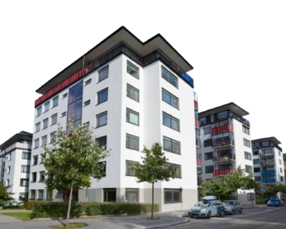Edificio residencial de varios pisos con árboles en la entrada, estacionamiento y ventanas grandes.