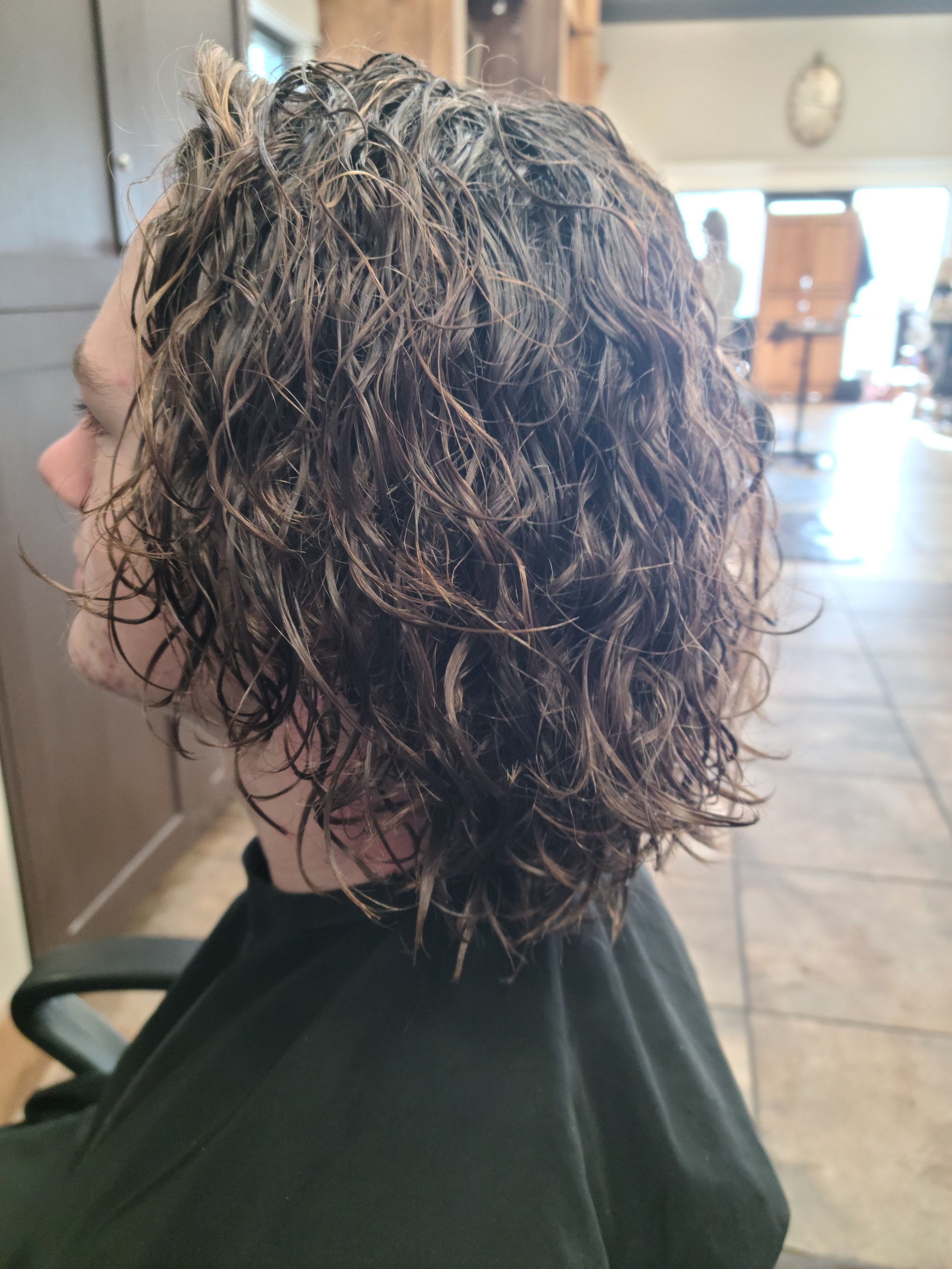 Close-up of a person's head with curly, wet hair, sitting in a salon or barber shop chair.