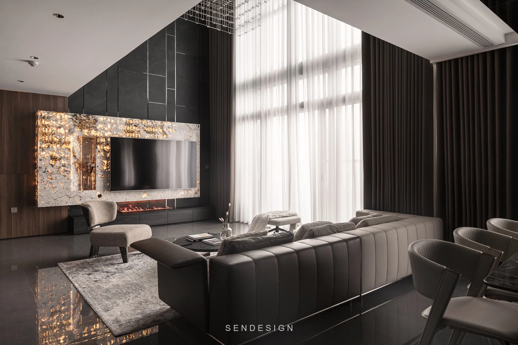 Modern living room with large windows, sheer curtains, dark wood and stone walls, contemporary furniture including a gray sofa and chairs, marble fireplace, area rug, and decorative ceiling features.