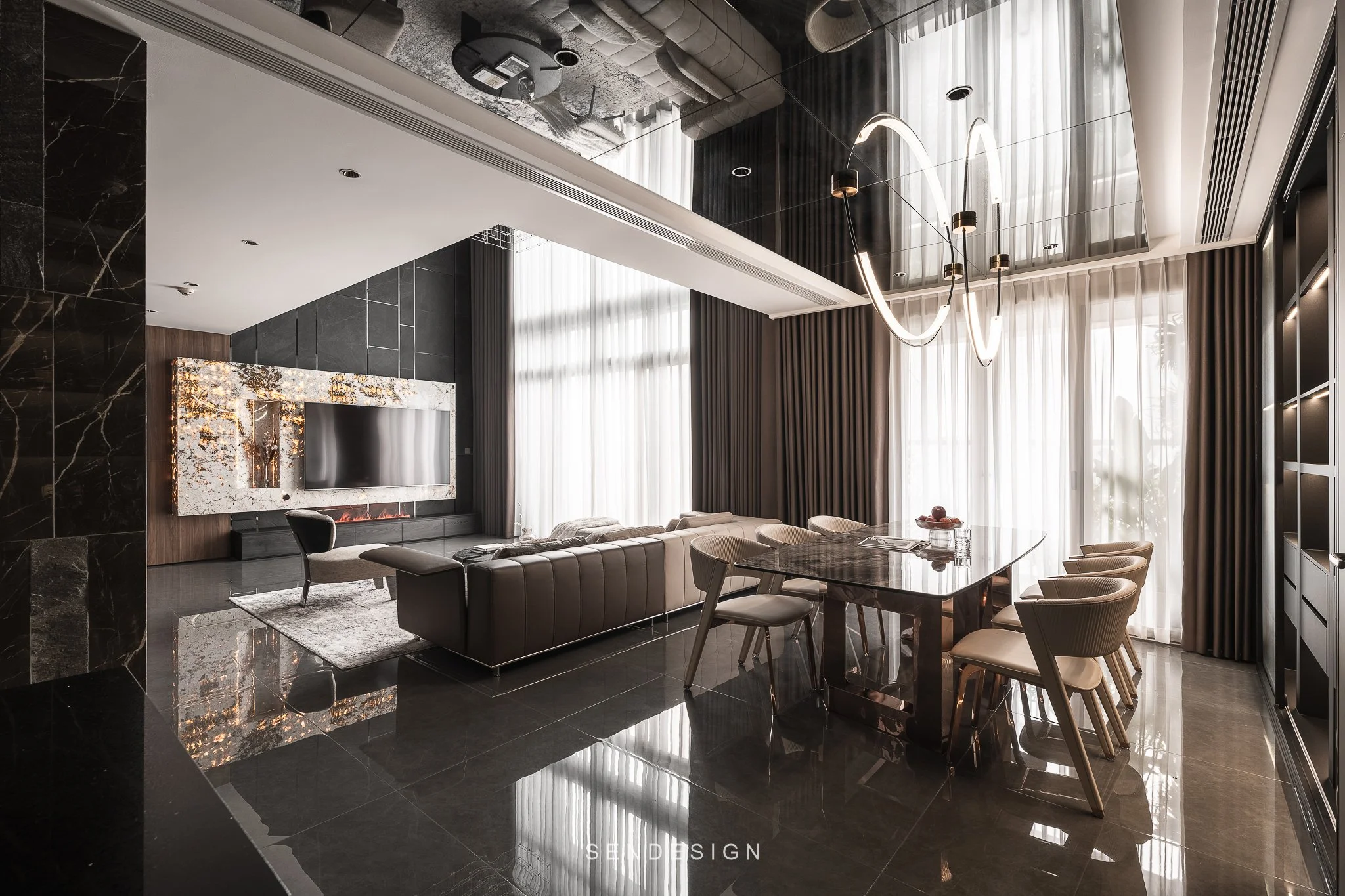 Modern living room with black marble flooring, a wall-mounted TV in a marble frame, a gray sofa, a circular chandelier, large windows with sheer curtains, and a dining table with beige chairs.
