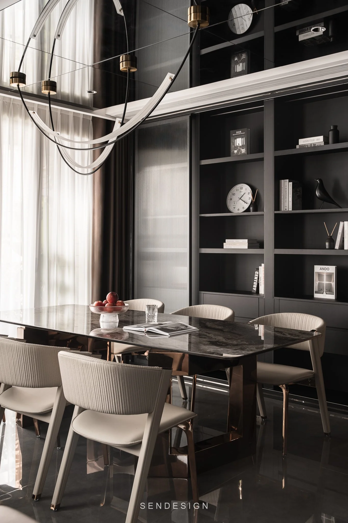 Modern dining room with a black marble table, white chairs, black shelving with books and decorative items, and a black ceiling with white curtains and a chandelier.
