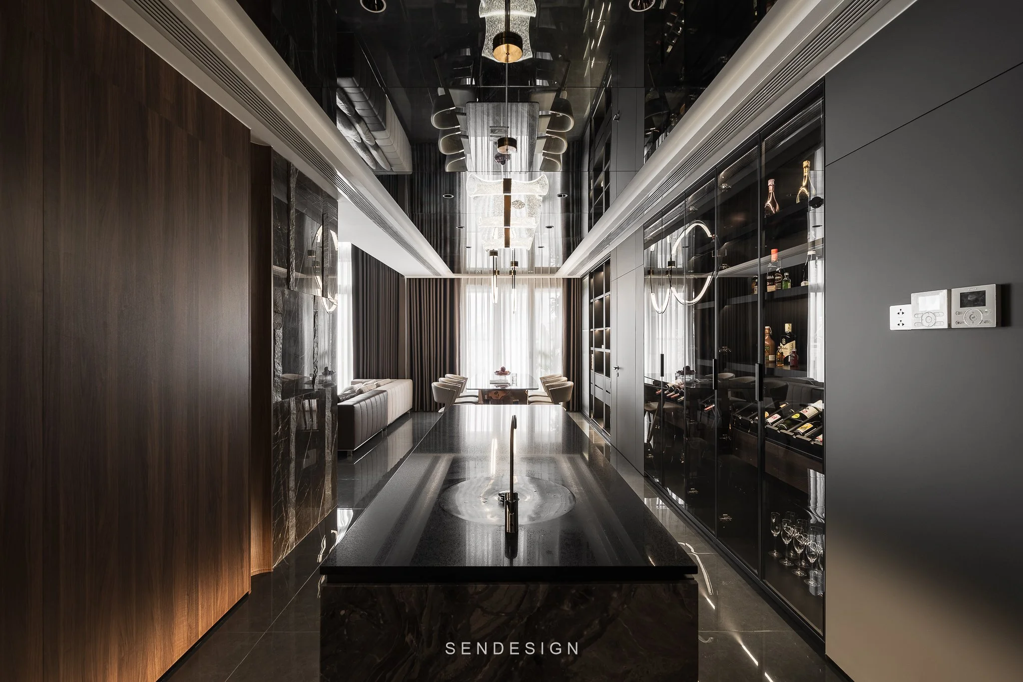Modern dining room with dark wood and black accents, featuring a black marble table, beige upholstered chairs, and a floor-to-ceiling glass wine cabinet with bottles and glasses, illuminated by contemporary light fixtures.